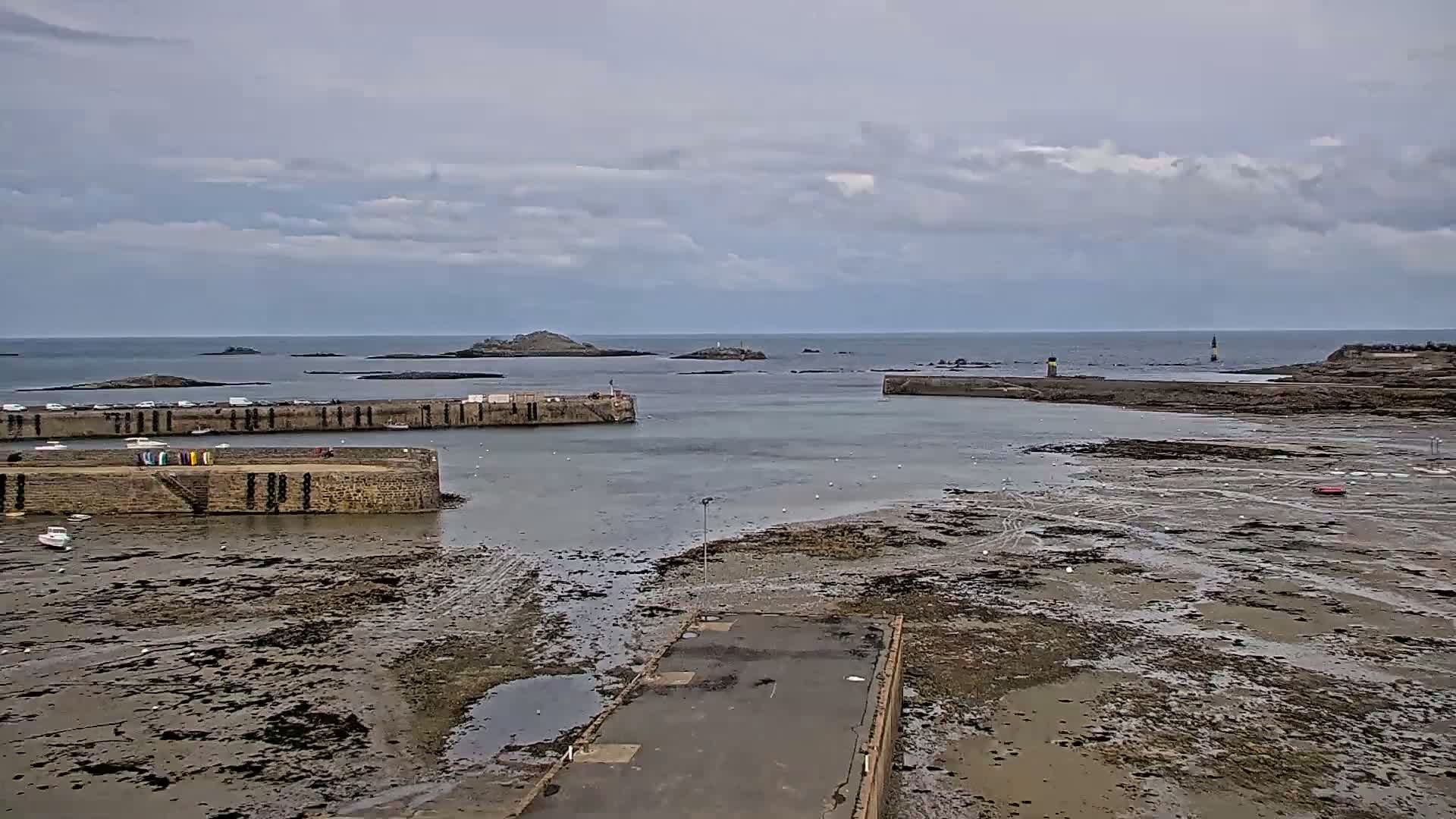 A stone harbor with boats is partially submerged at low tide under a cloudy sky.