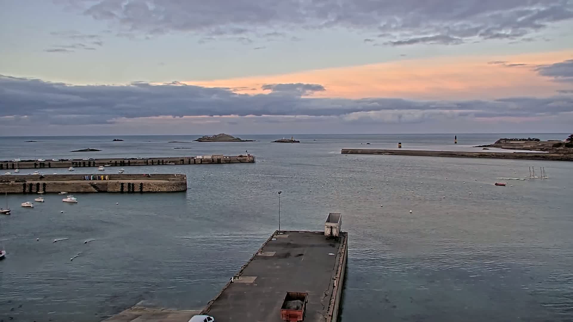 A harbor with several small boats is seen at sunset under a partly cloudy sky.