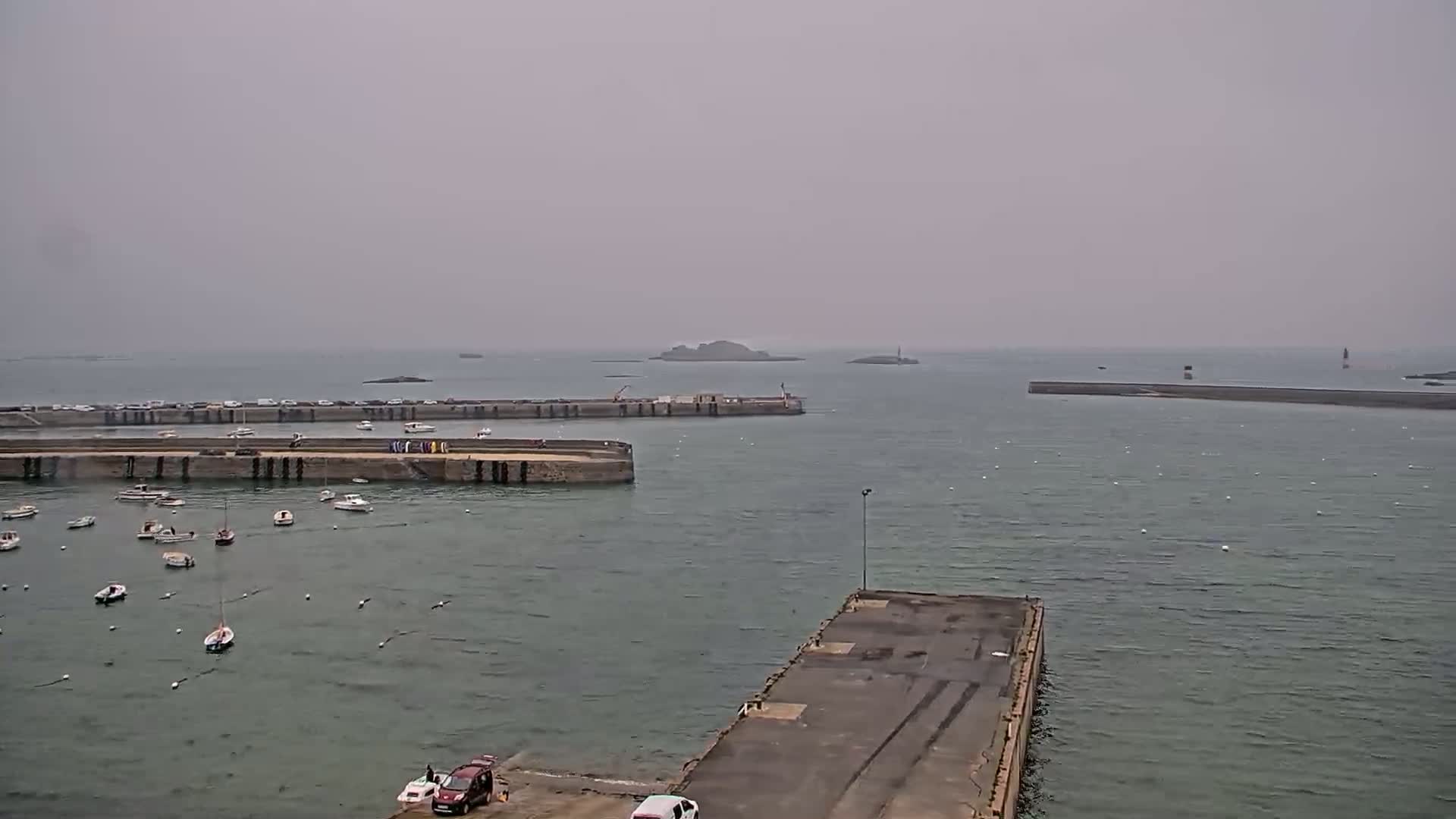 A harbor filled with small boats under an overcast sky, with a larger body of water and small islands visible in the distance.