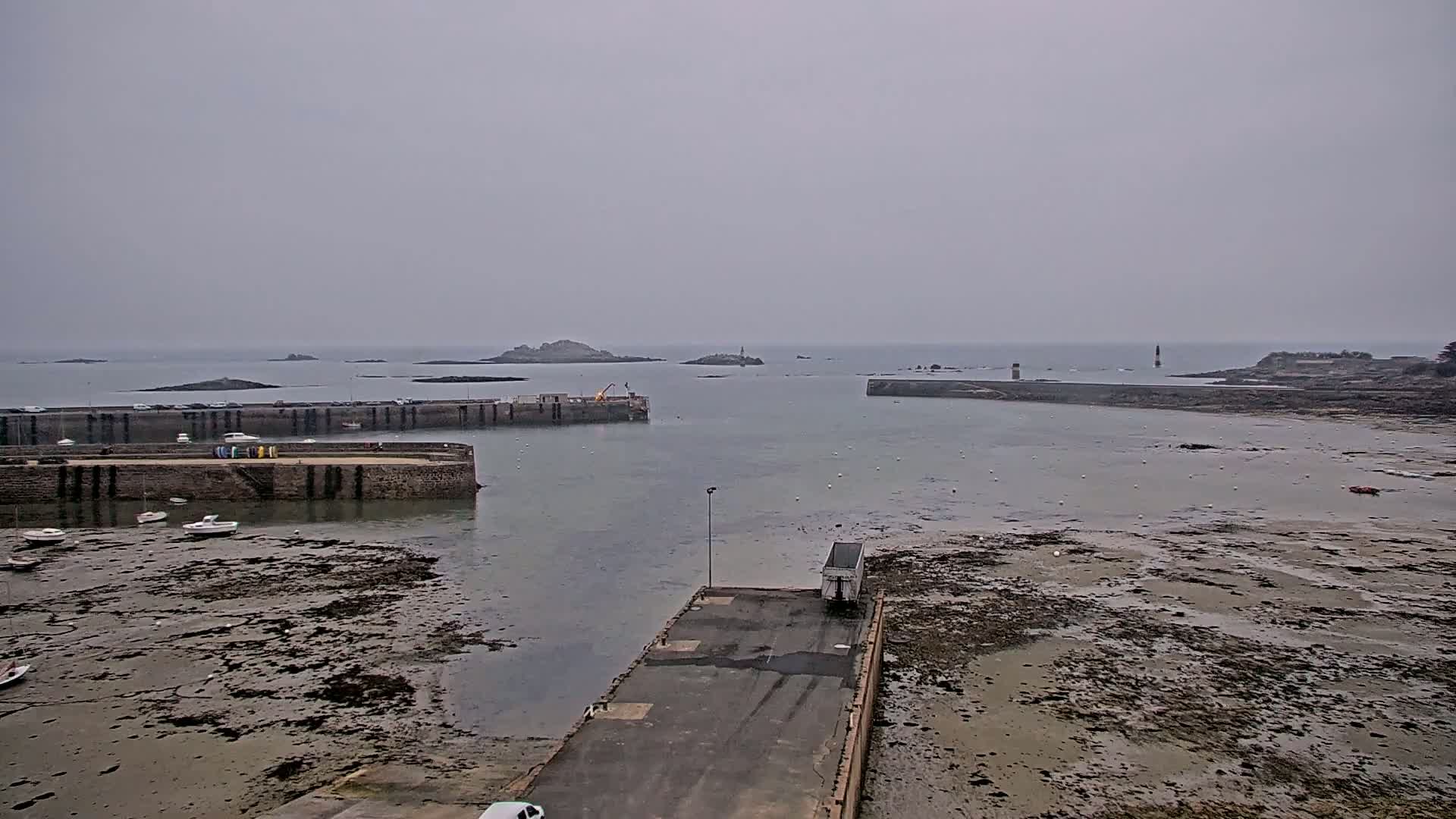 A harbor with low tide, showing boats and a small dock under an overcast sky.