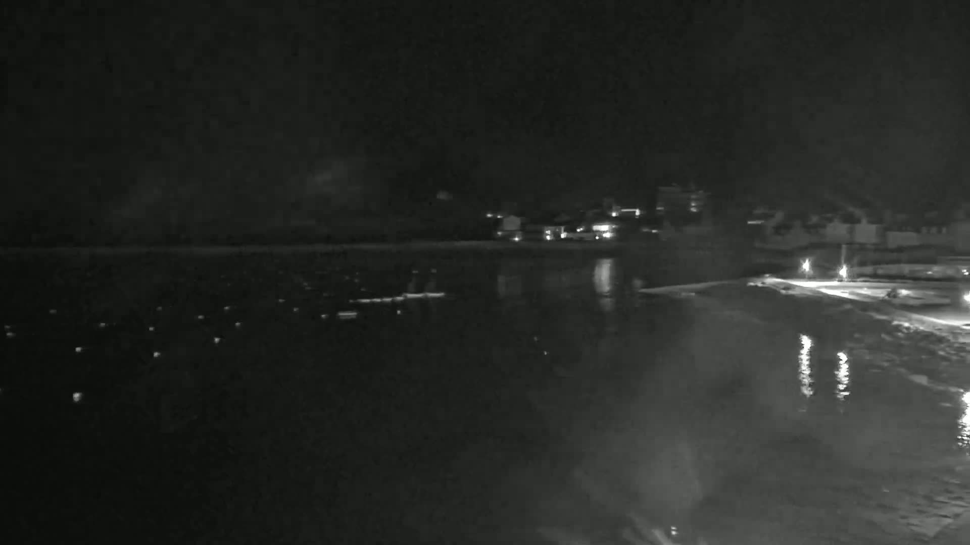 A nighttime view of a dark body of water with faintly lit buildings across the shore under a dark sky.