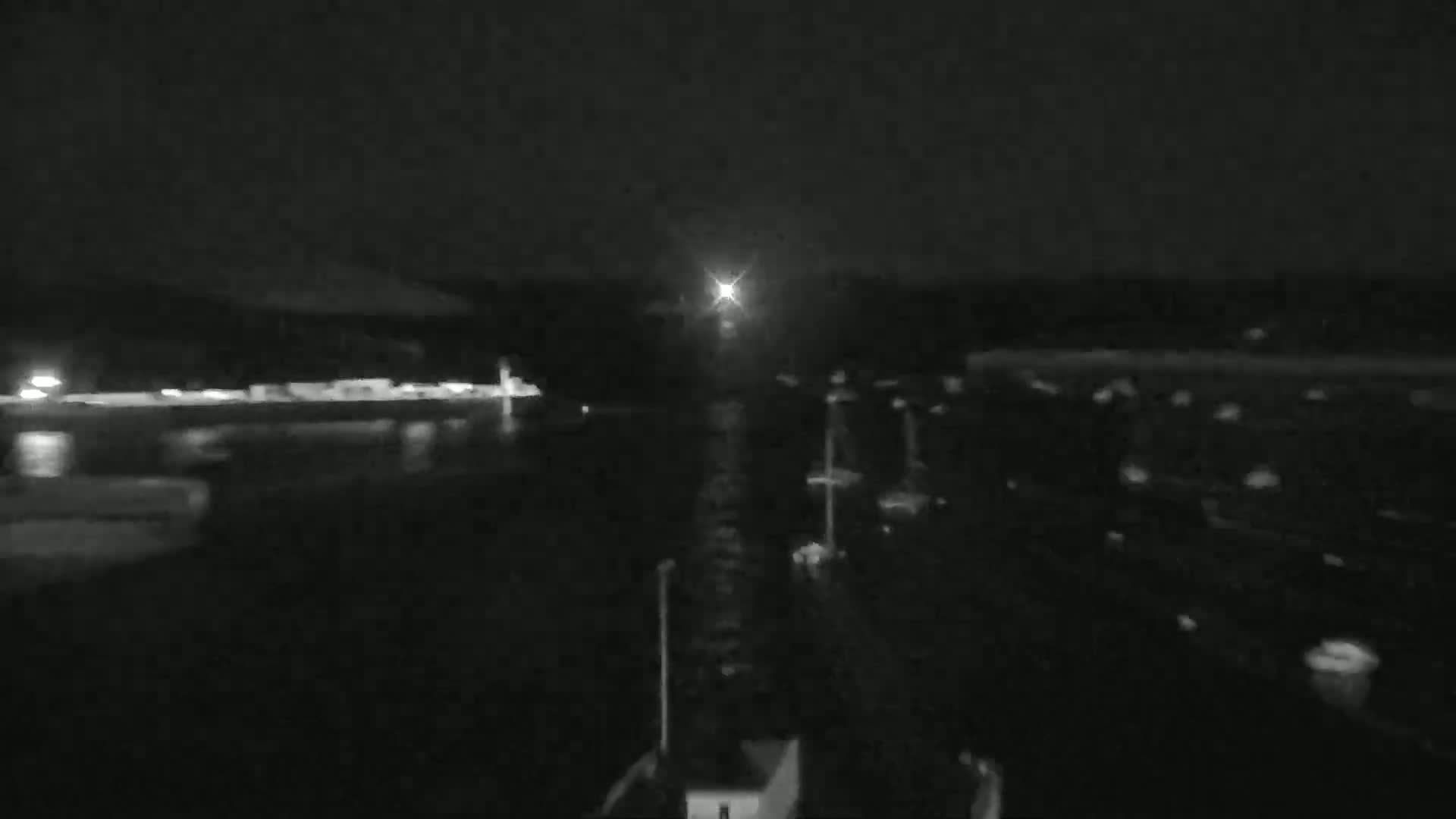 A nighttime view of a dark body of water with faintly visible boats and a bright light in the distance.