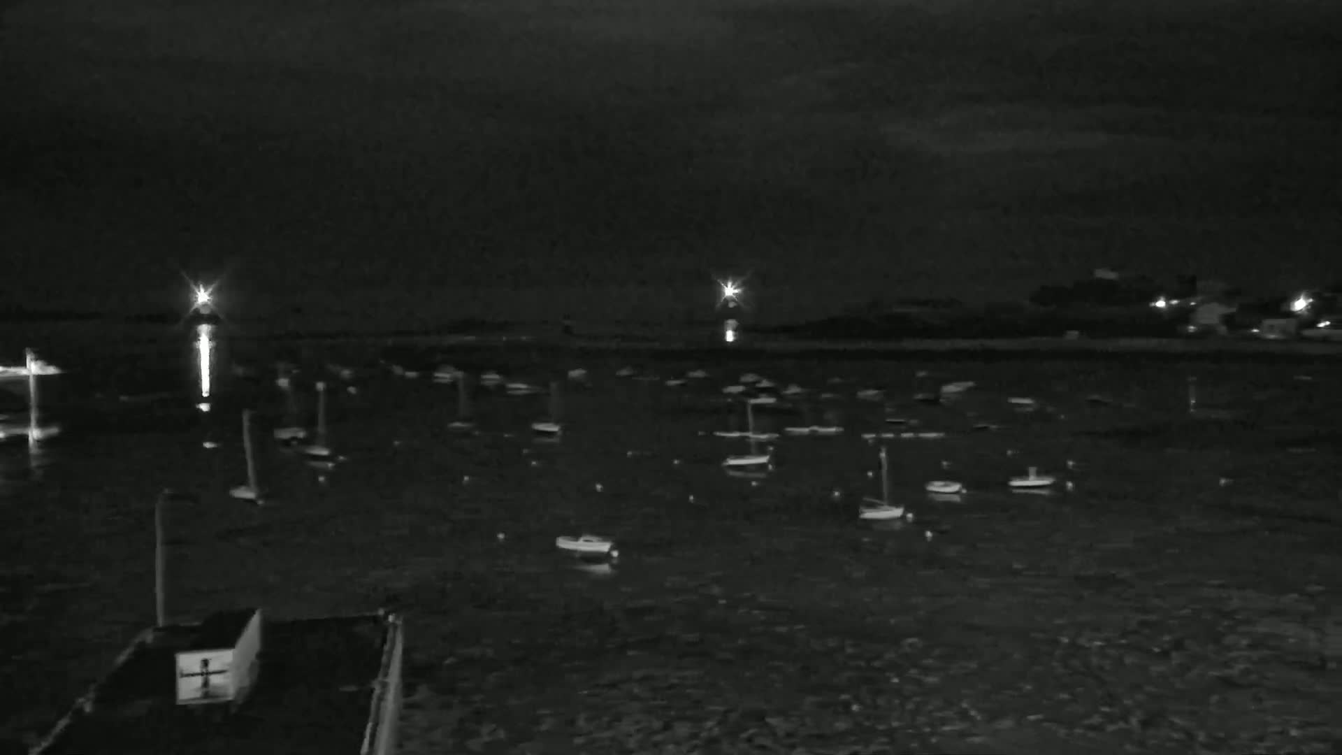 Numerous small boats are moored in a dark body of water at night, illuminated by distant lights.
