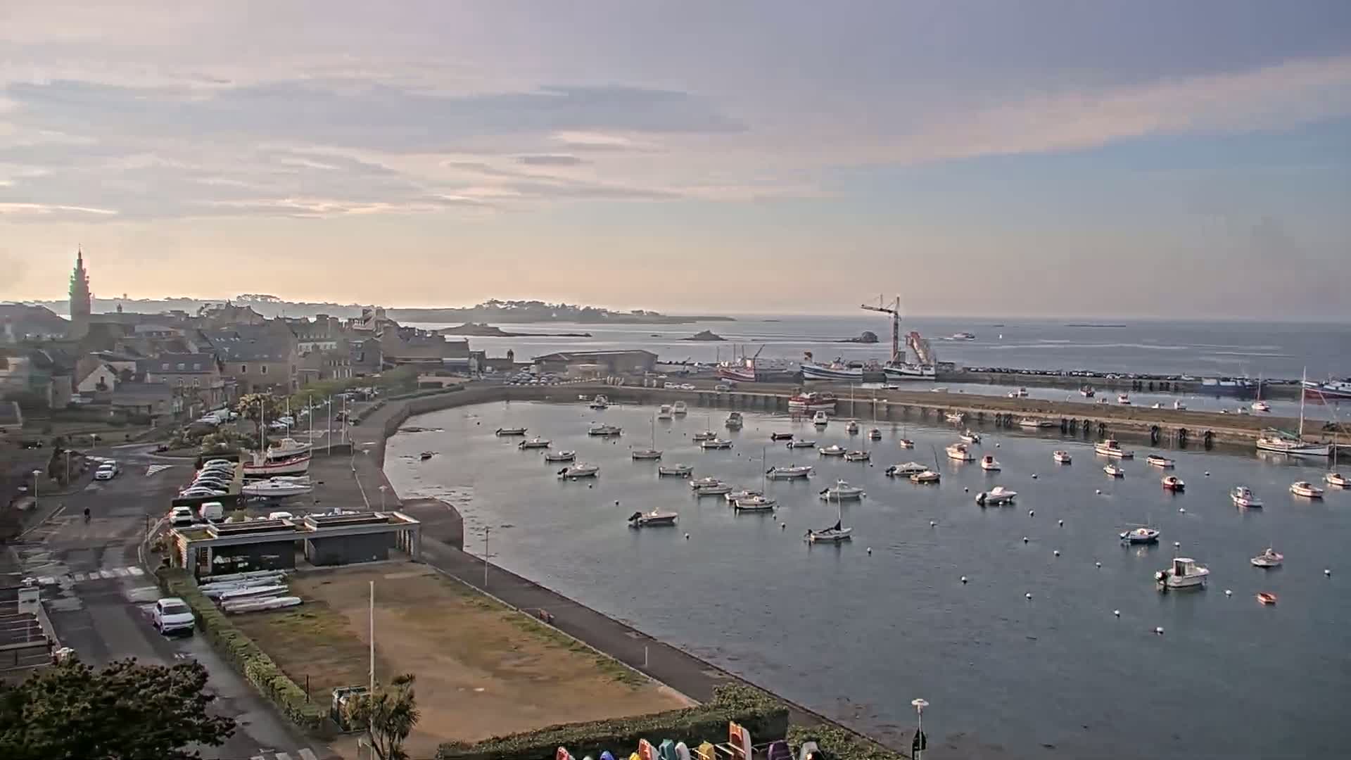A harbor filled with numerous boats is situated next to a town under a partly cloudy sky.