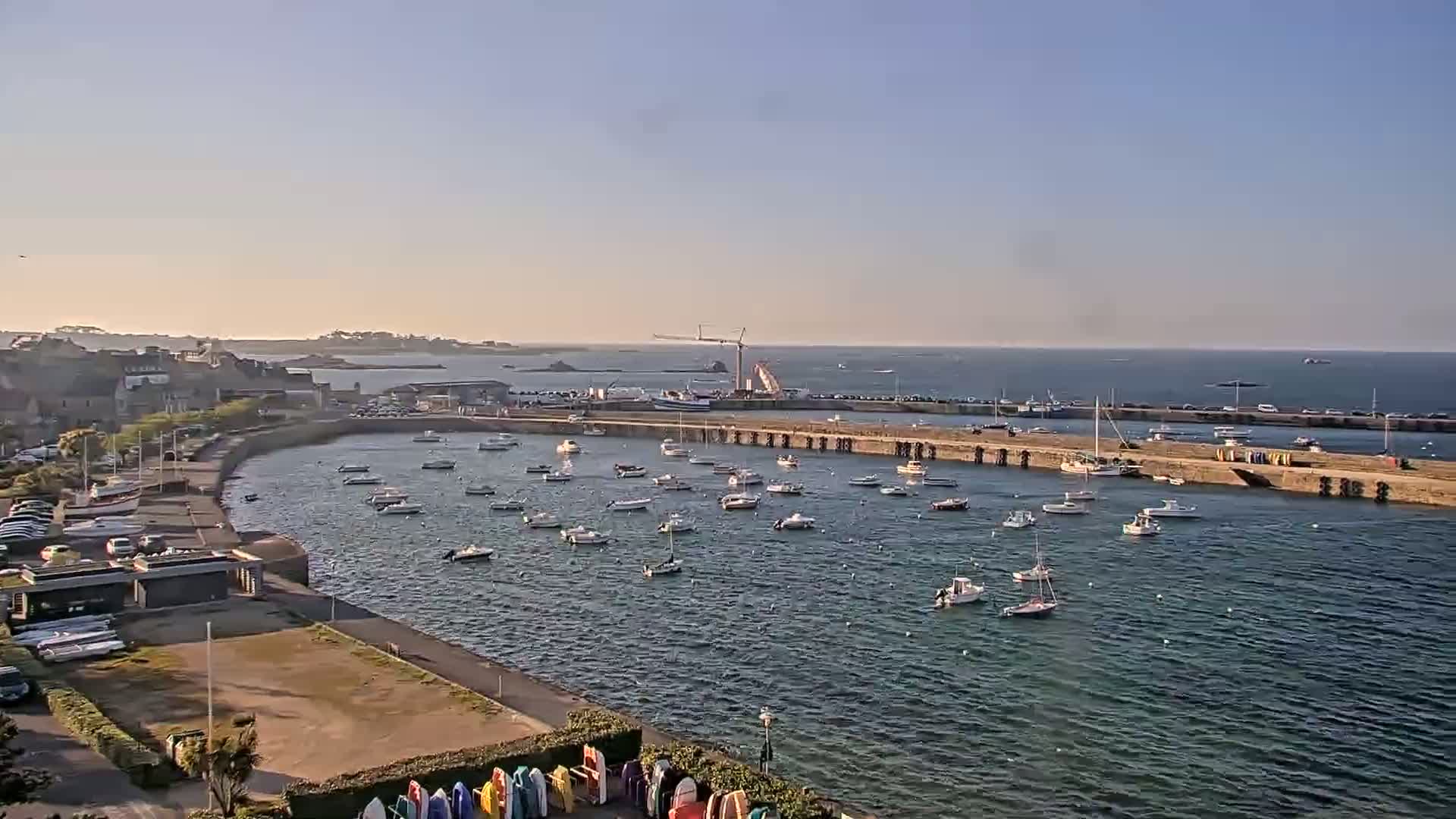 A harbor filled with numerous small boats under a clear, sunny sky, next to a town and a larger body of water.