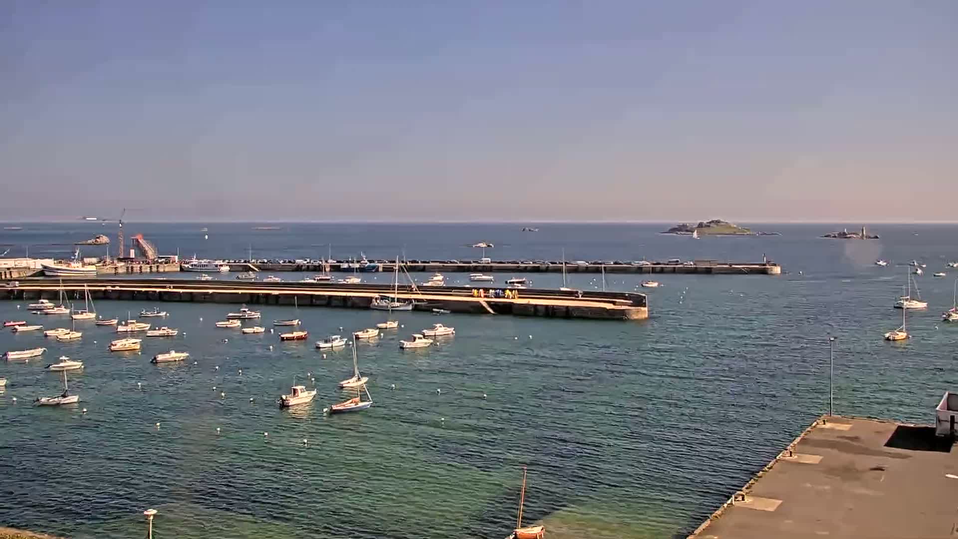 A harbor filled with numerous small boats under a clear, sunny sky, with a small island visible in the distance.