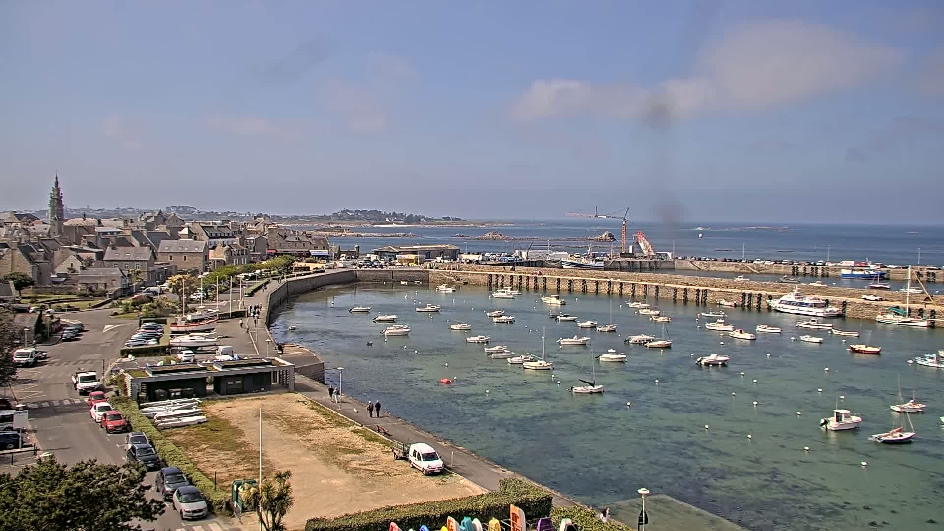 A coastal town with a harbor filled with numerous boats under a mostly sunny sky.