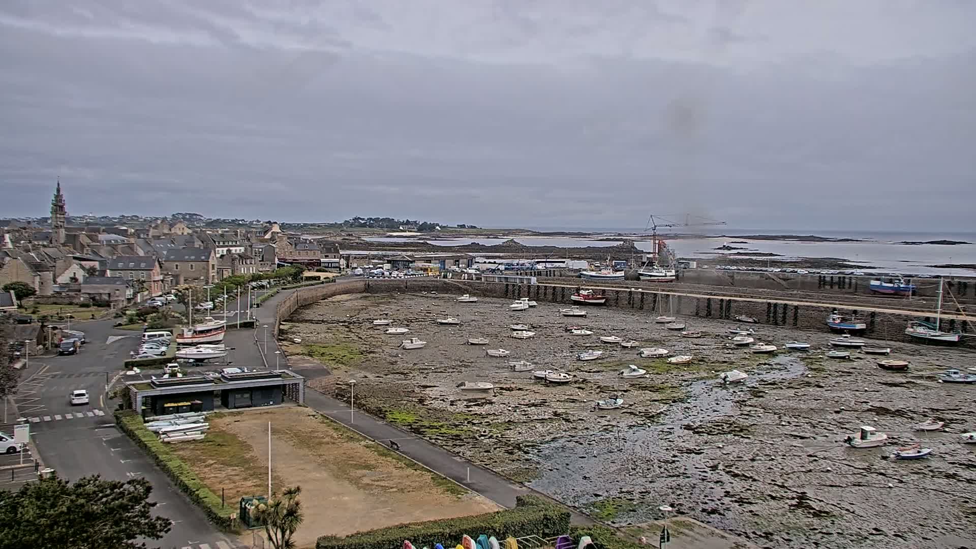 A coastal town with numerous small boats resting on a mudflat harbor at low tide under an overcast sky.