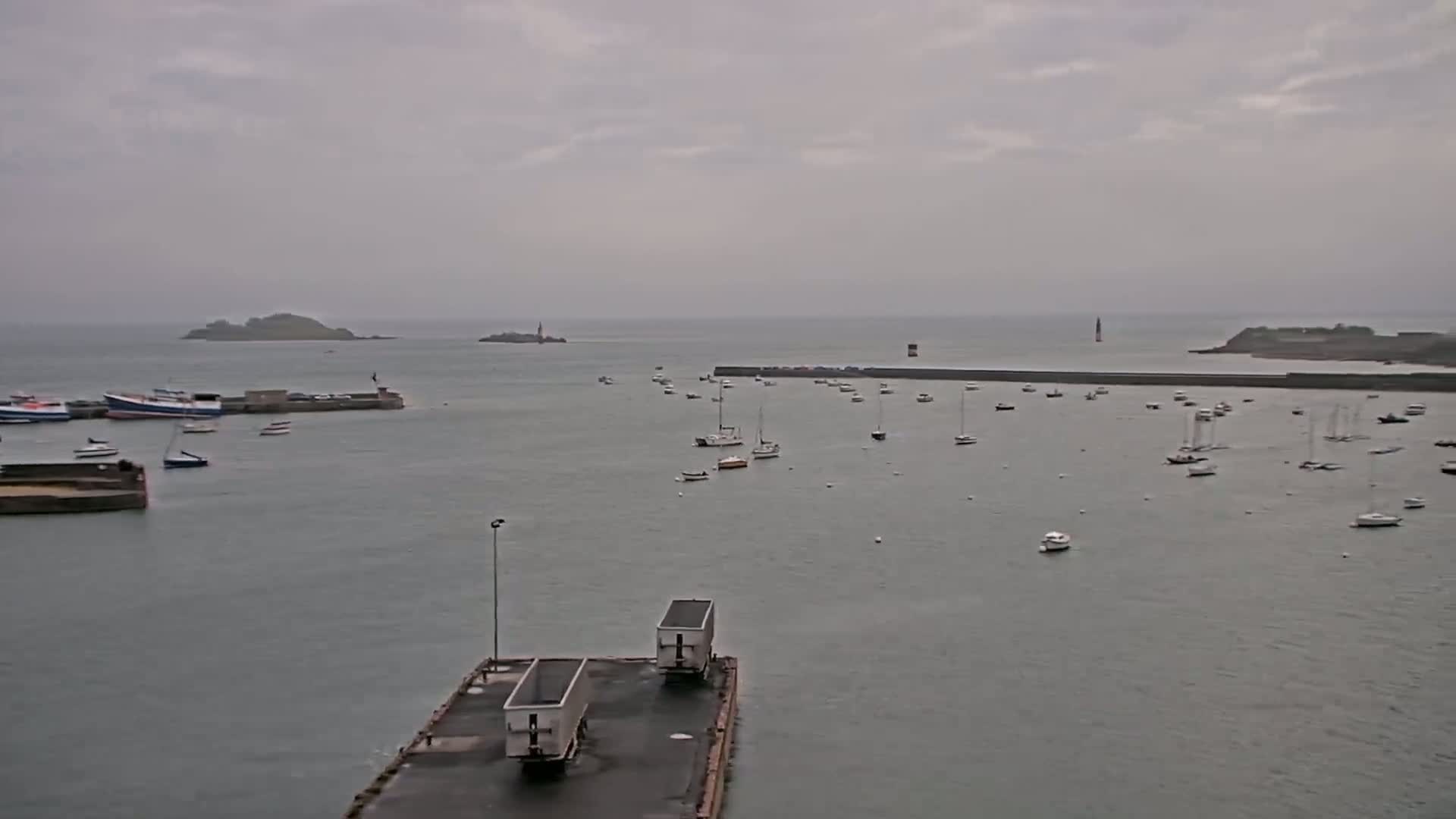 A harbor filled with numerous small boats under an overcast sky, with two islands visible in the distance.