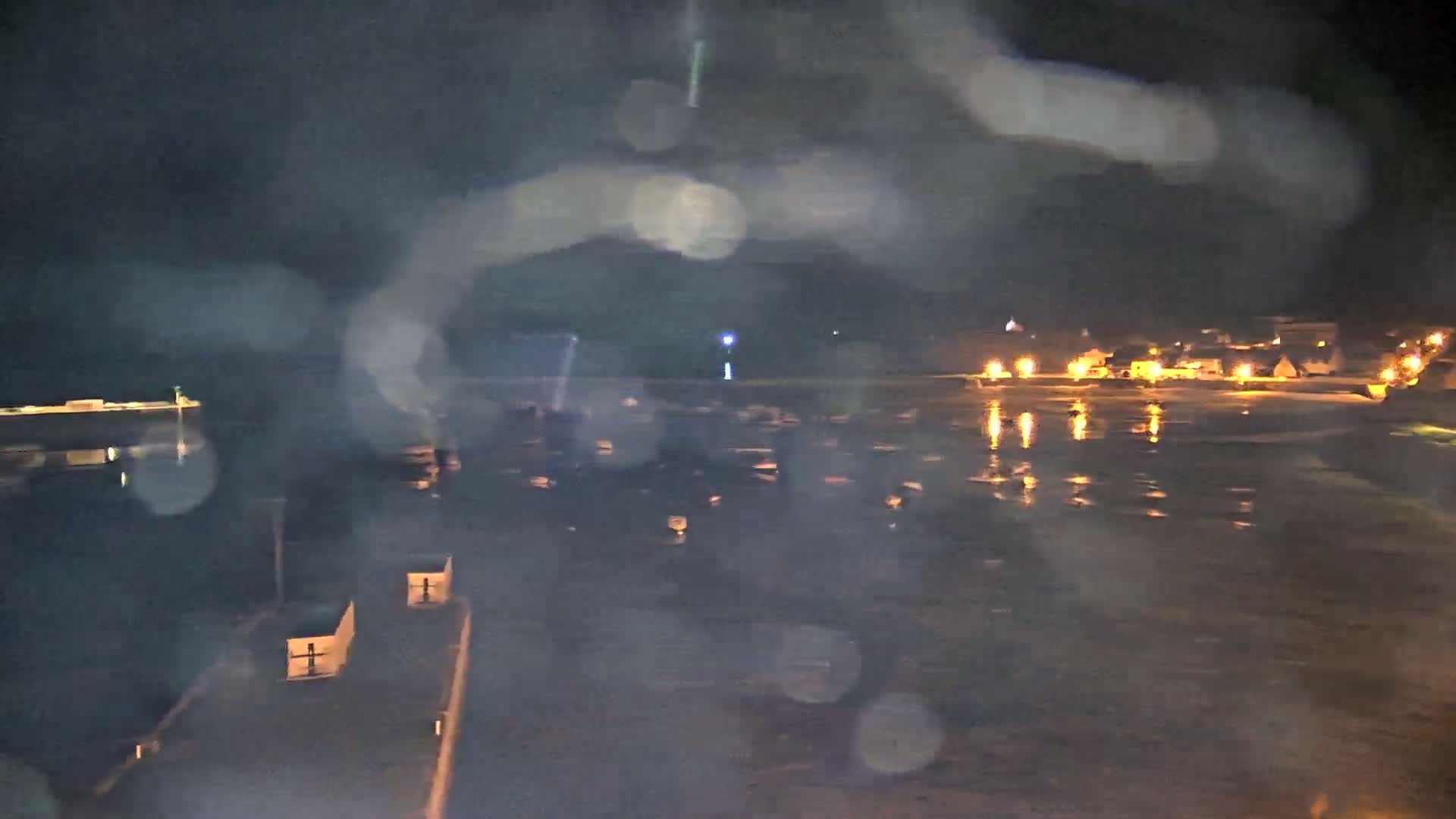 A nighttime view of a rain-streaked, water-filled harbor with a small, lit town in the background.