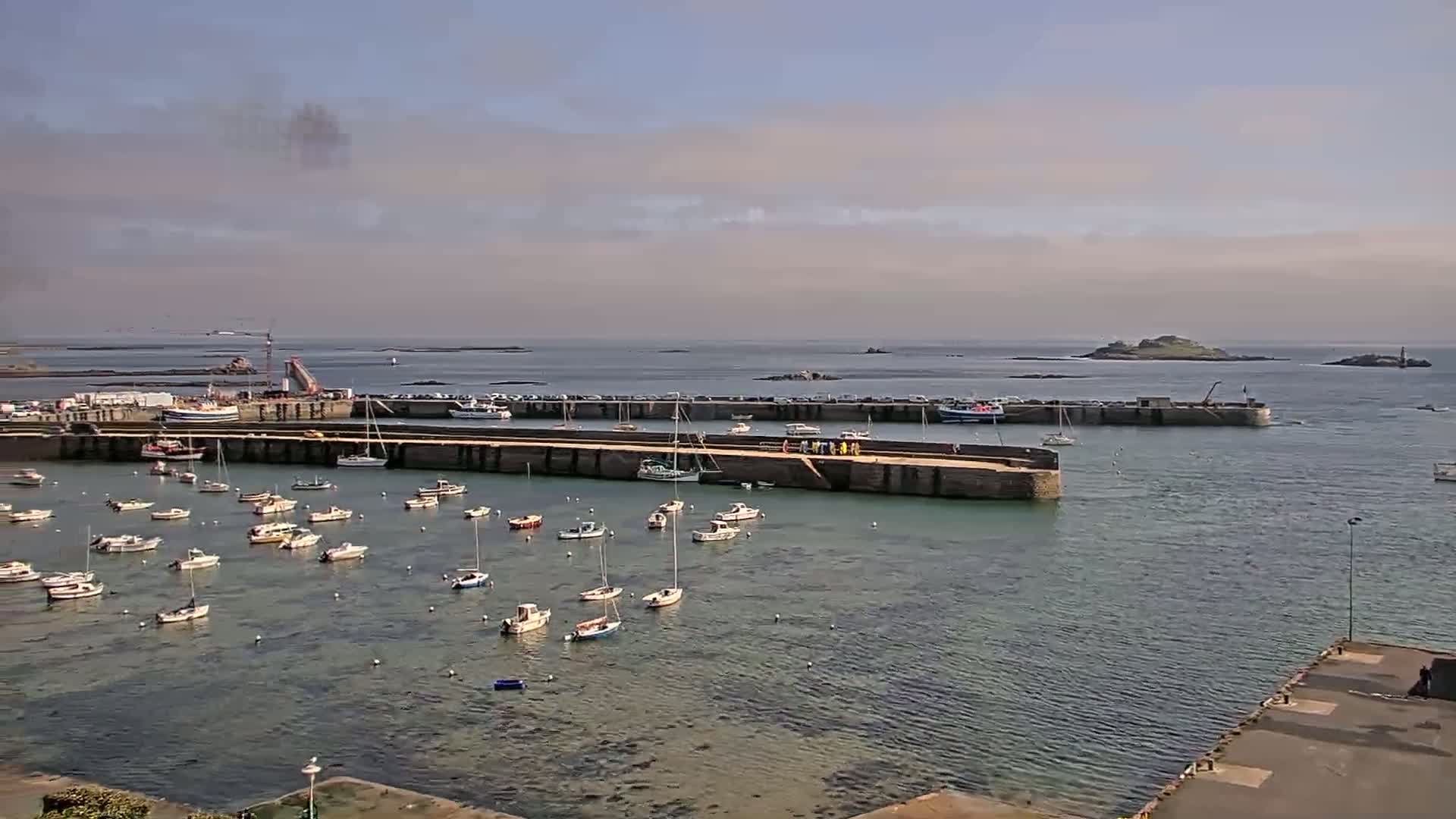 A harbor filled with numerous small boats under a partly cloudy sky, with islands visible in the distance.
