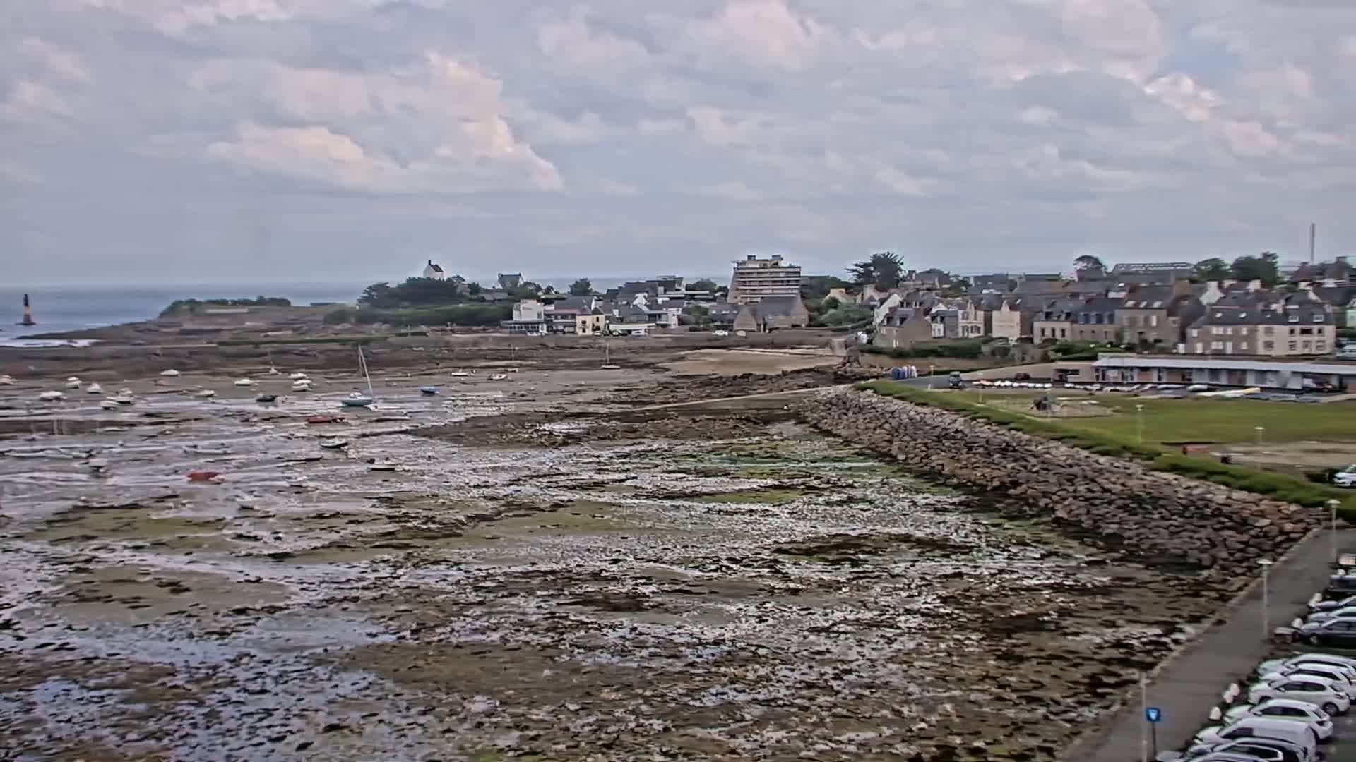 A coastal town under a cloudy sky, with numerous small boats resting on exposed tidal flats.