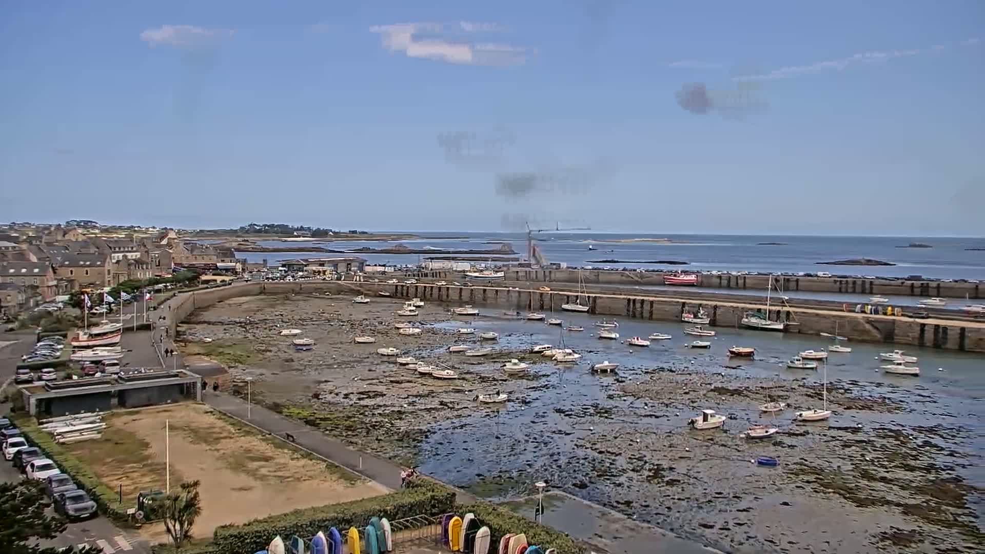 A coastal town with numerous small boats in a harbor at low tide under a mostly sunny sky.