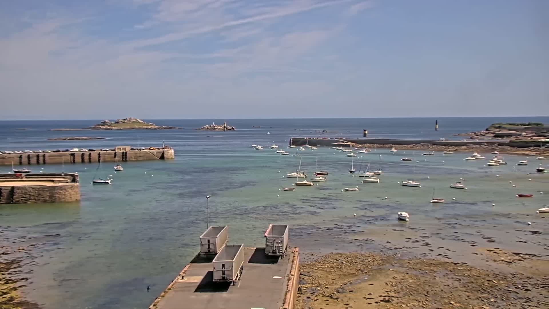 A harbor filled with numerous small boats under a sunny sky, with several islands visible in the distance.