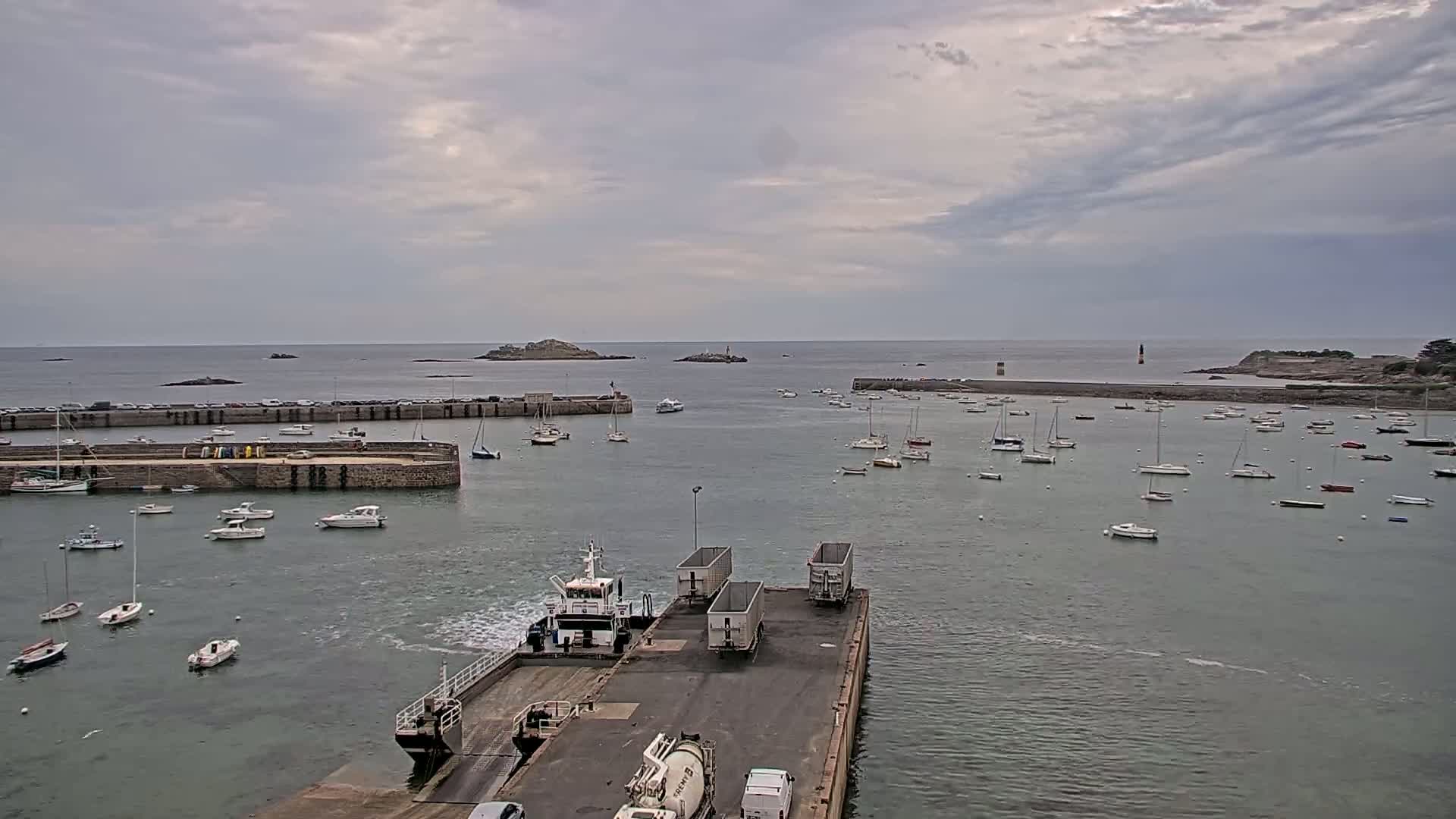 A ferry approaches a harbor filled with numerous sailboats and small motorboats under a cloudy sky.