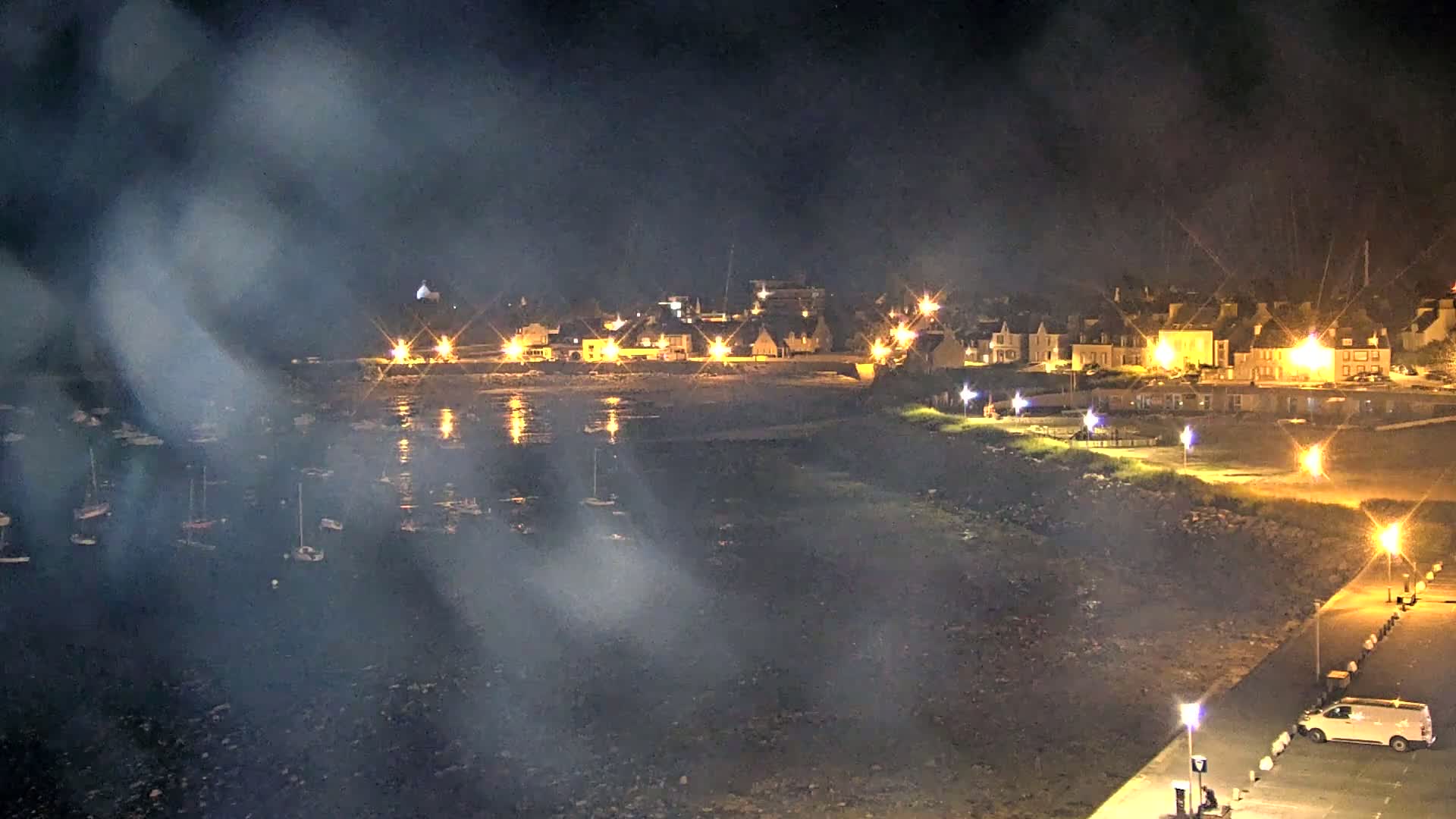 A hazy night scene shows a small, illuminated town beside a harbor filled with boats.
