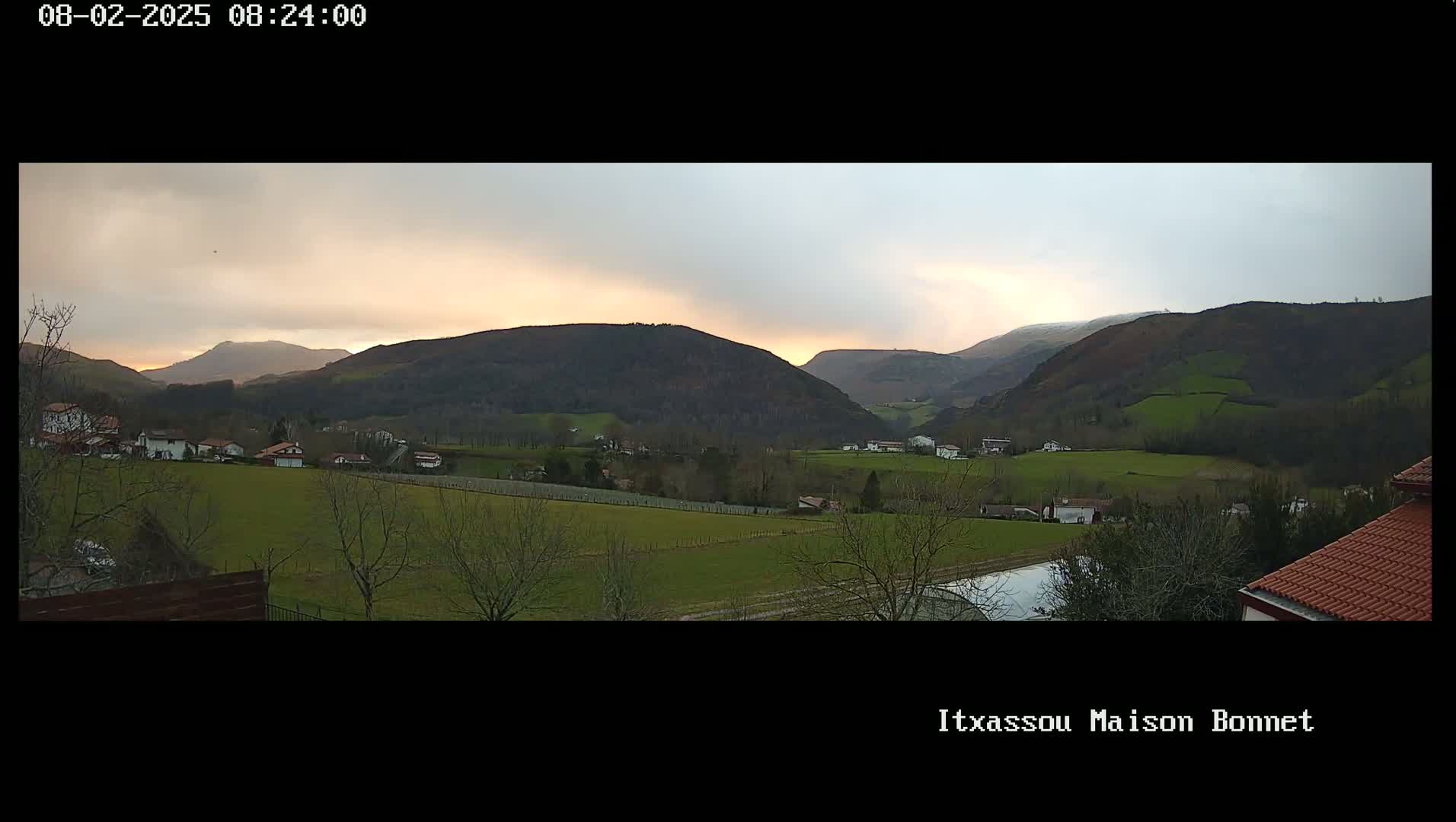 A valley with houses and farmlands, nestled between rolling hills under a partly cloudy, dusky sky.