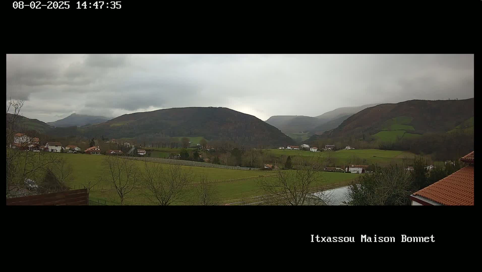 A view of a rural valley under an overcast sky, showing houses, farmland, and rolling hills in the distance.