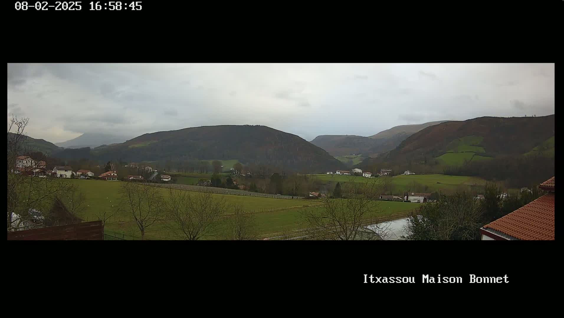 A sprawling green valley dotted with houses and trees under a cloudy sky, with rolling hills in the background.