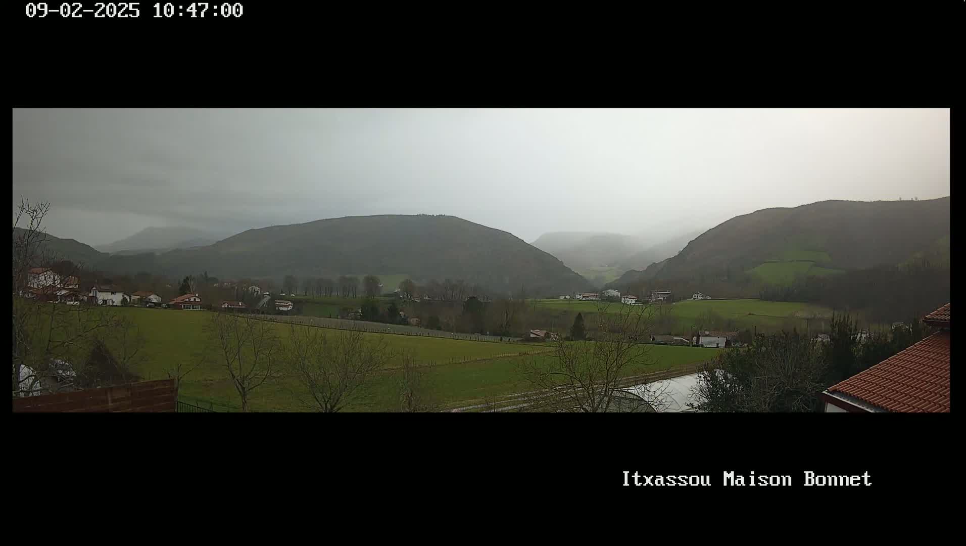 A sprawling, overcast valley dotted with small houses and farmland is visible under a gray sky.