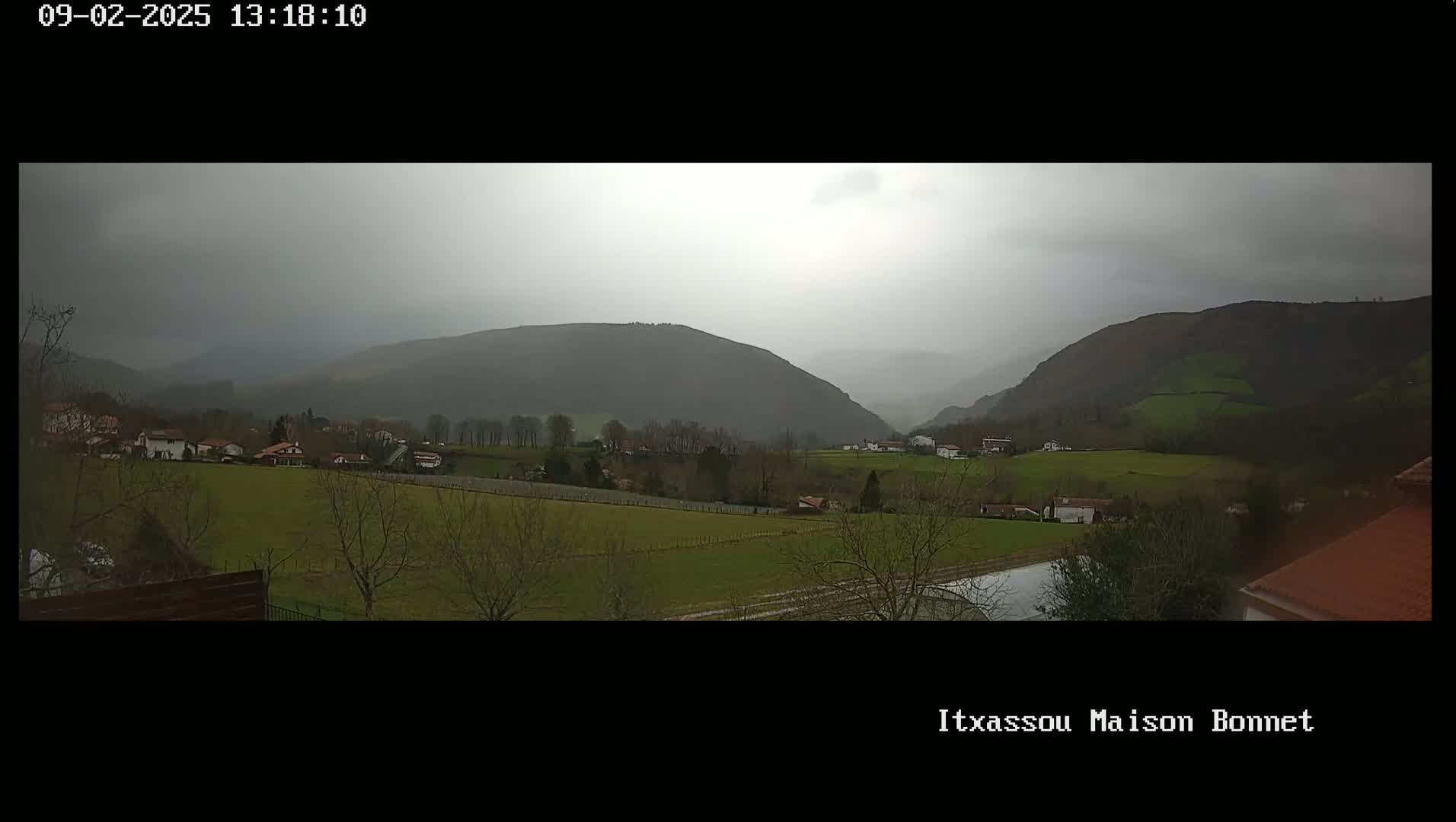 A hazy, overcast day reveals a valley of green fields and small buildings nestled between rolling hills.