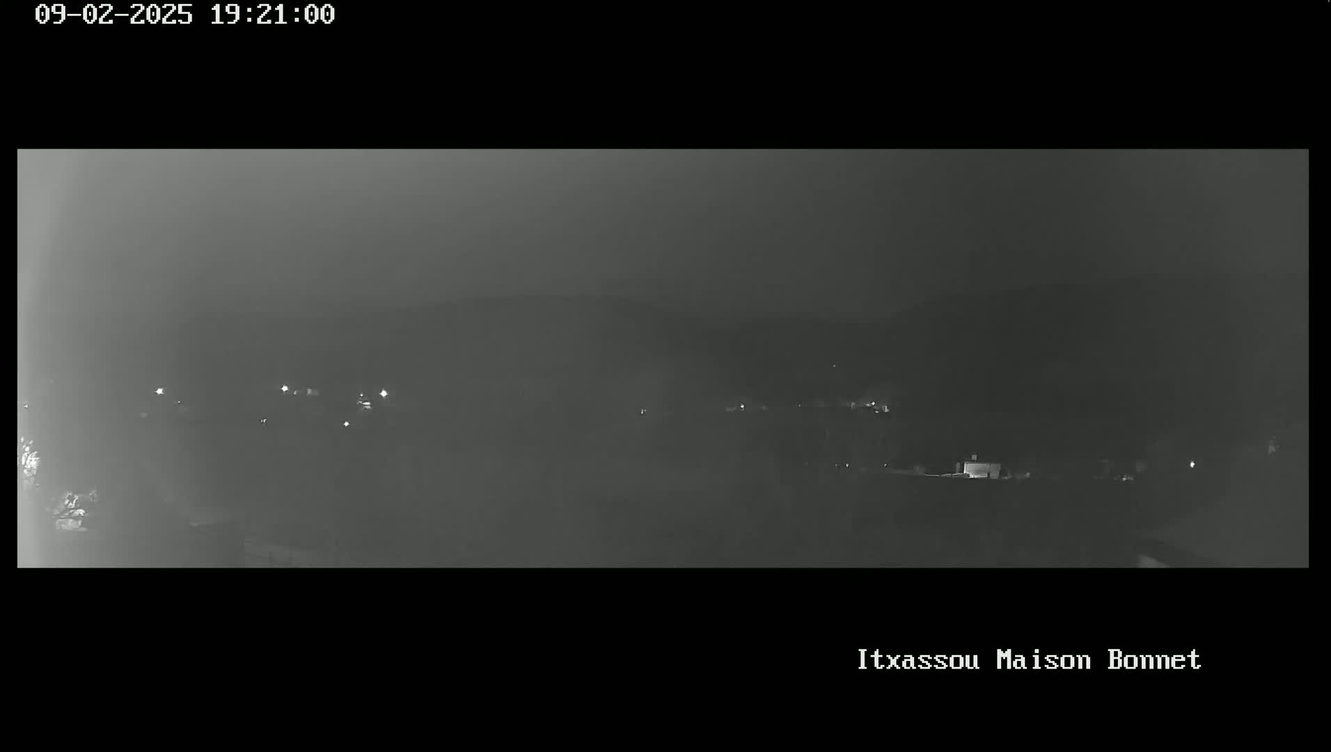 A nighttime, hazy view shows a dark landscape with sparse, faint lights in the distance.