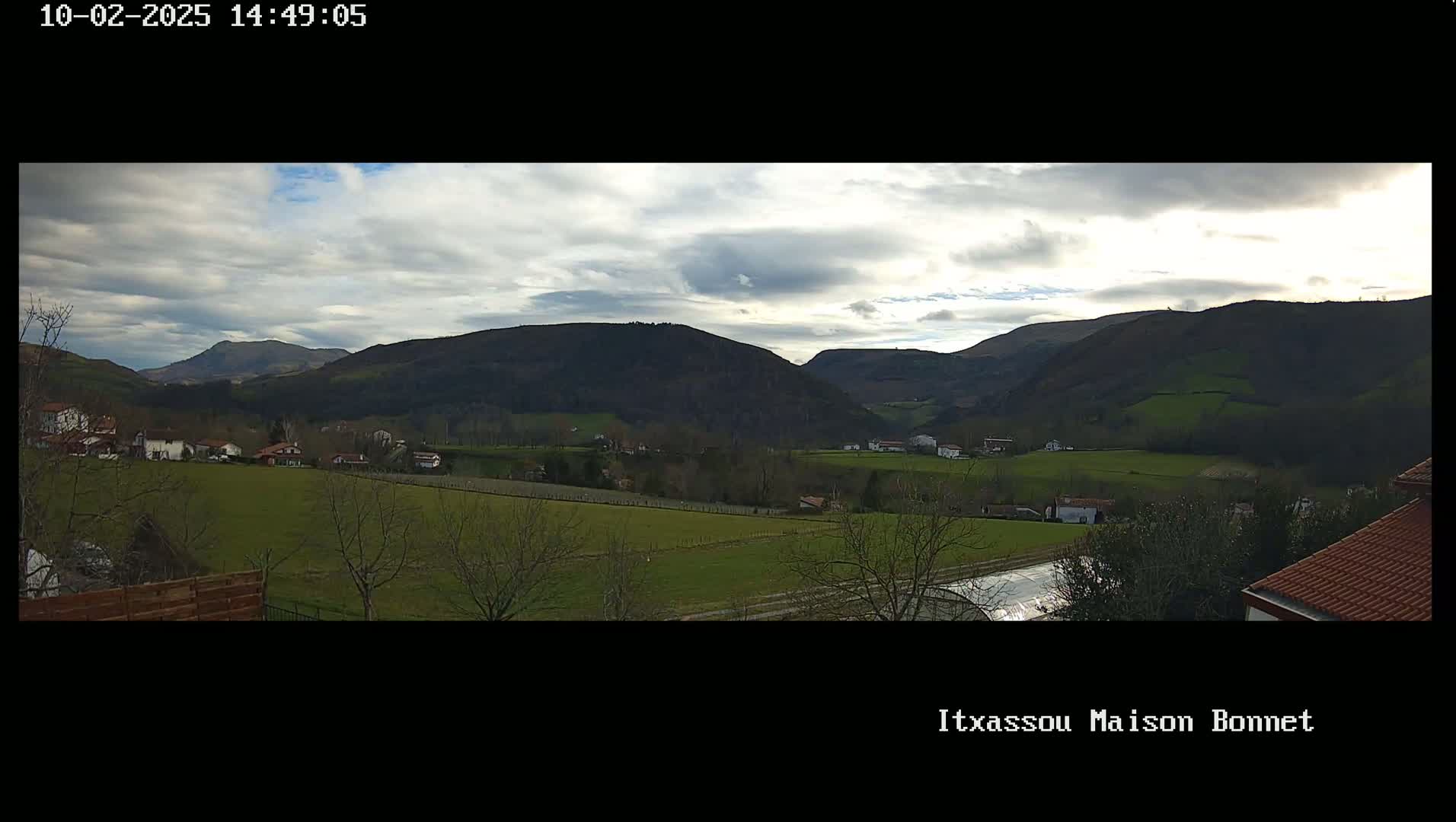 A partly cloudy day reveals a valley of green fields and scattered houses nestled between rolling hills.