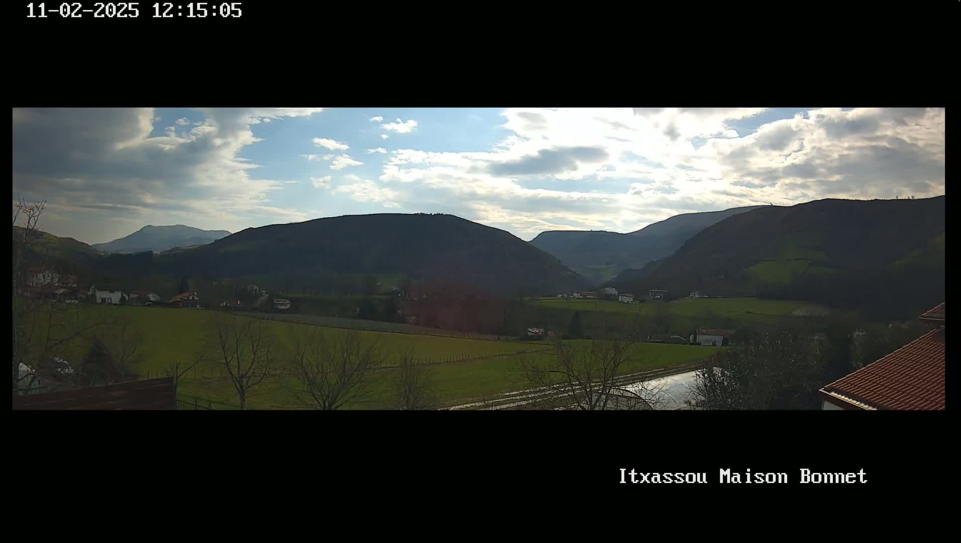 A partly cloudy day reveals a panoramic view of rolling green hills and a valley dotted with houses, under a mostly clear sky.