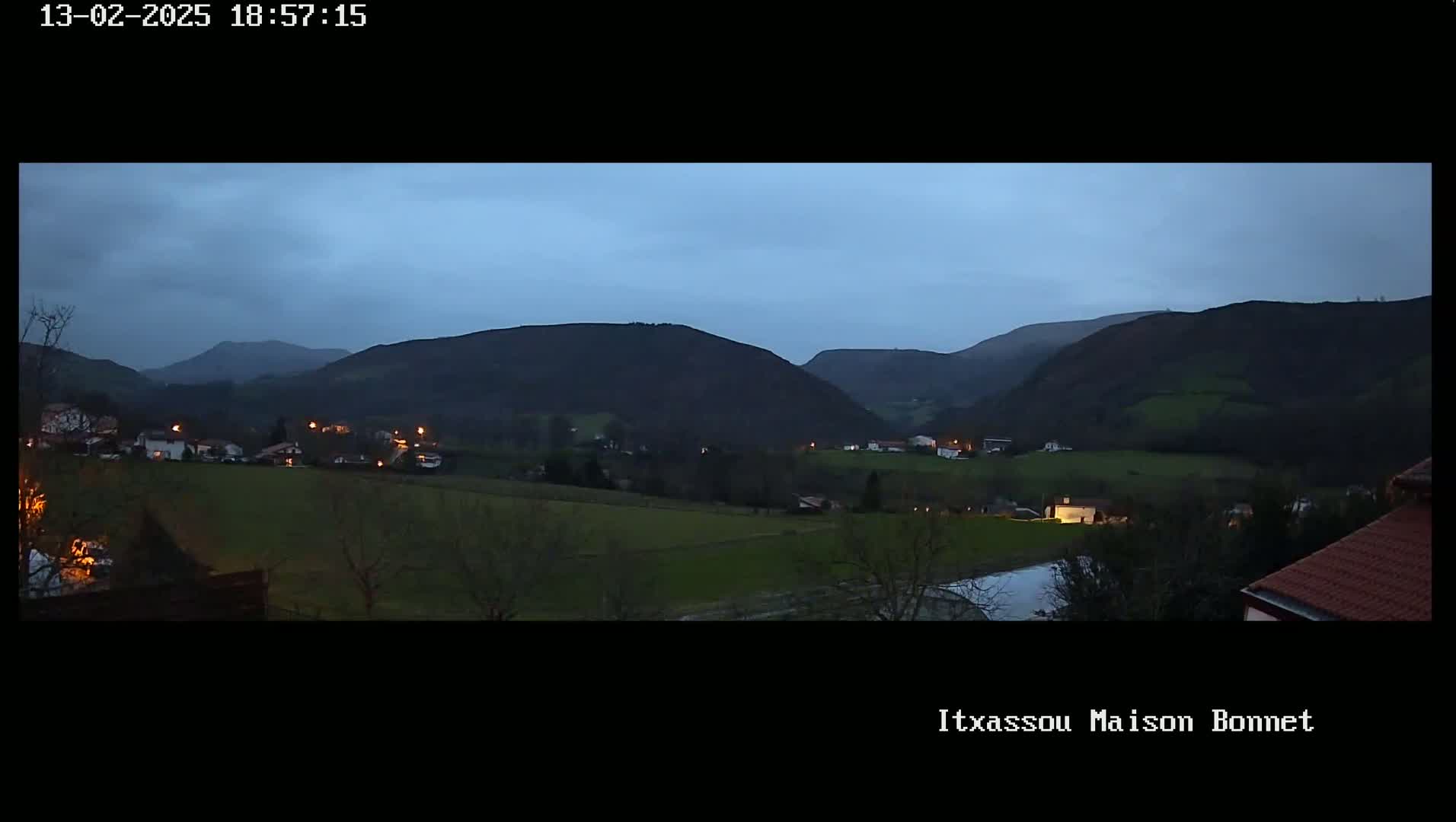 A twilight view shows a valley with a small village nestled amongst dark green hills under a dusky blue sky.