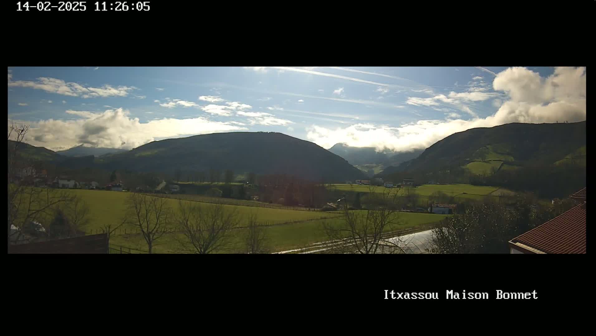 A partly cloudy day reveals a valley of green fields and dark, rolling hills.