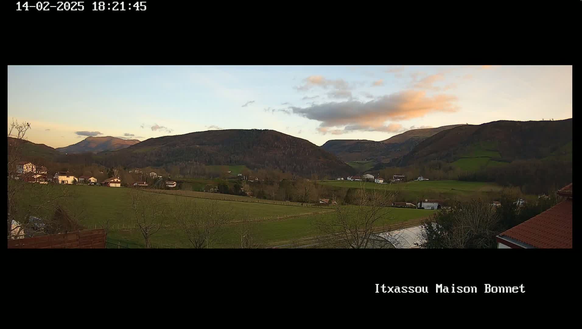 A tranquil valley with houses and farmland under a partly cloudy, sunset sky.