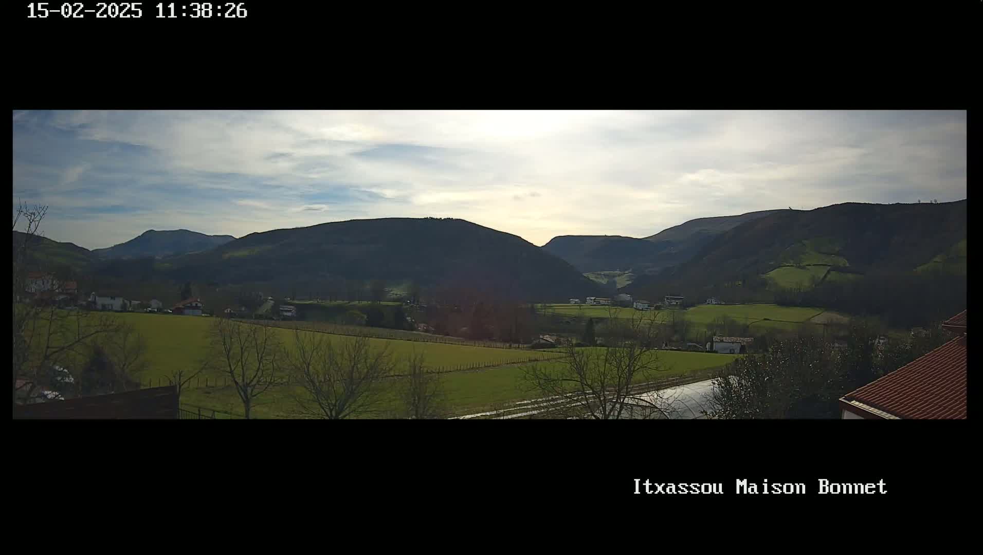 A panoramic view shows a partly cloudy sky over a valley of green fields and dark, rolling hills.