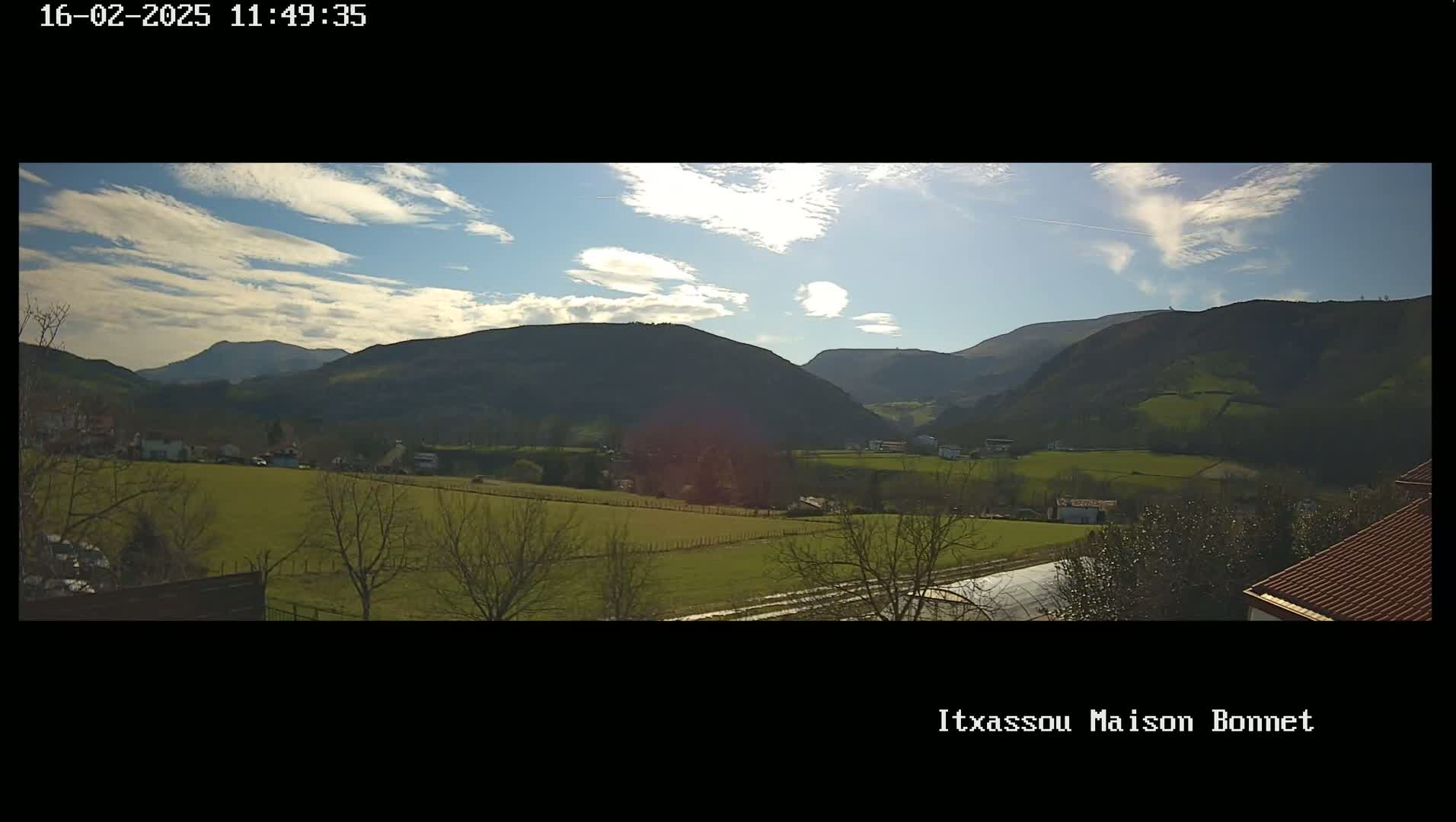 A sunny day with scattered clouds overlooks a verdant valley nestled between rolling hills.