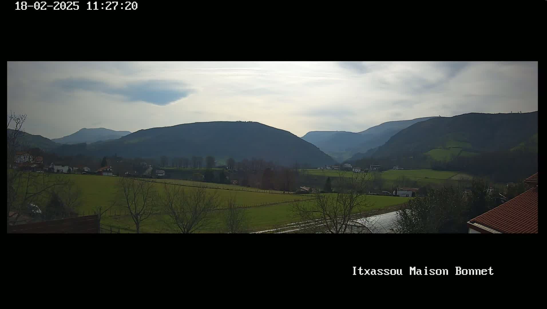A panoramic view of rolling green hills and mountains under a mostly cloudy sky.