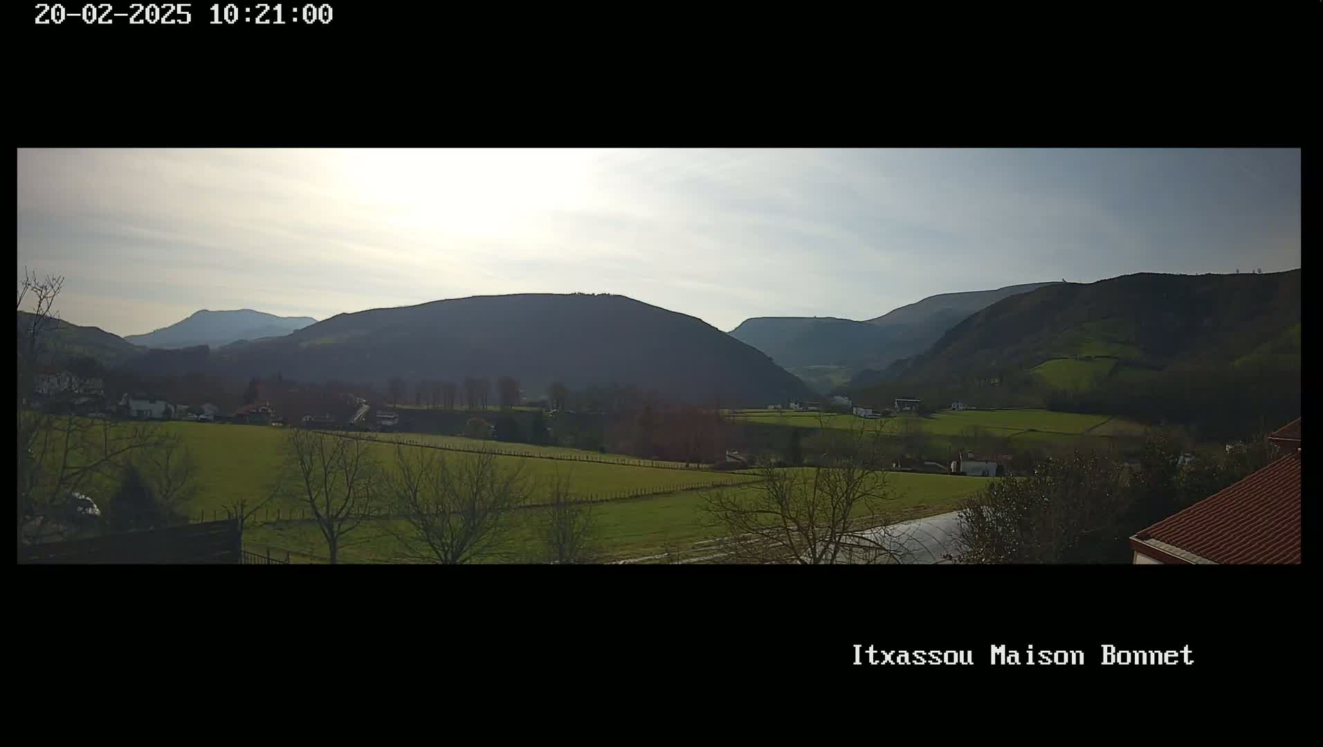 A sunny day reveals a valley of green fields and sparse trees nestled between rolling hills and mountains.