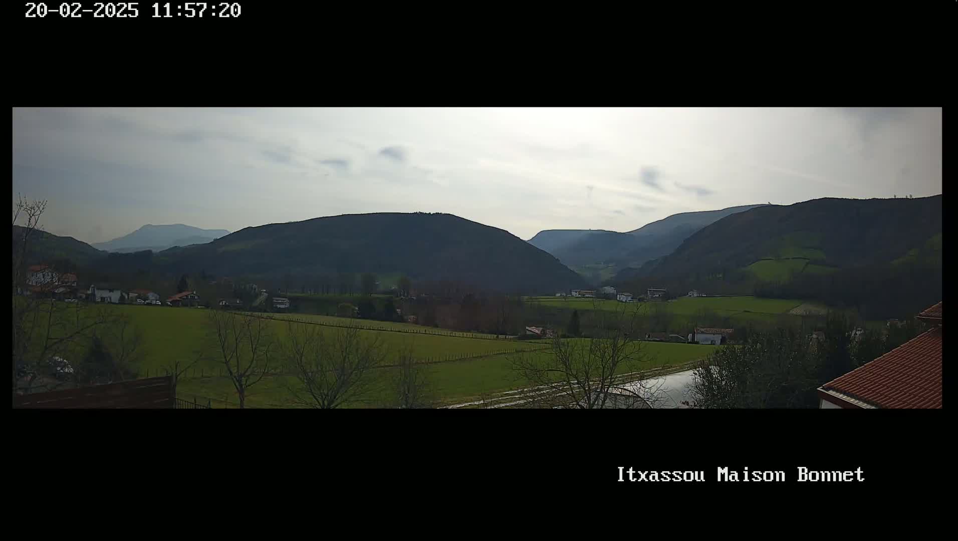 A panoramic view of a verdant valley nestled between rolling hills under a mostly cloudy sky.