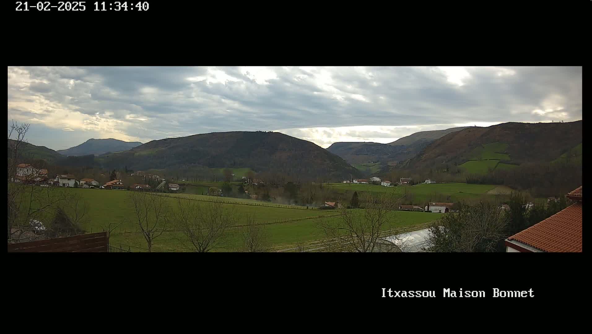 A partly cloudy day reveals a pastoral valley with rolling green hills, sparsely populated with houses and trees.