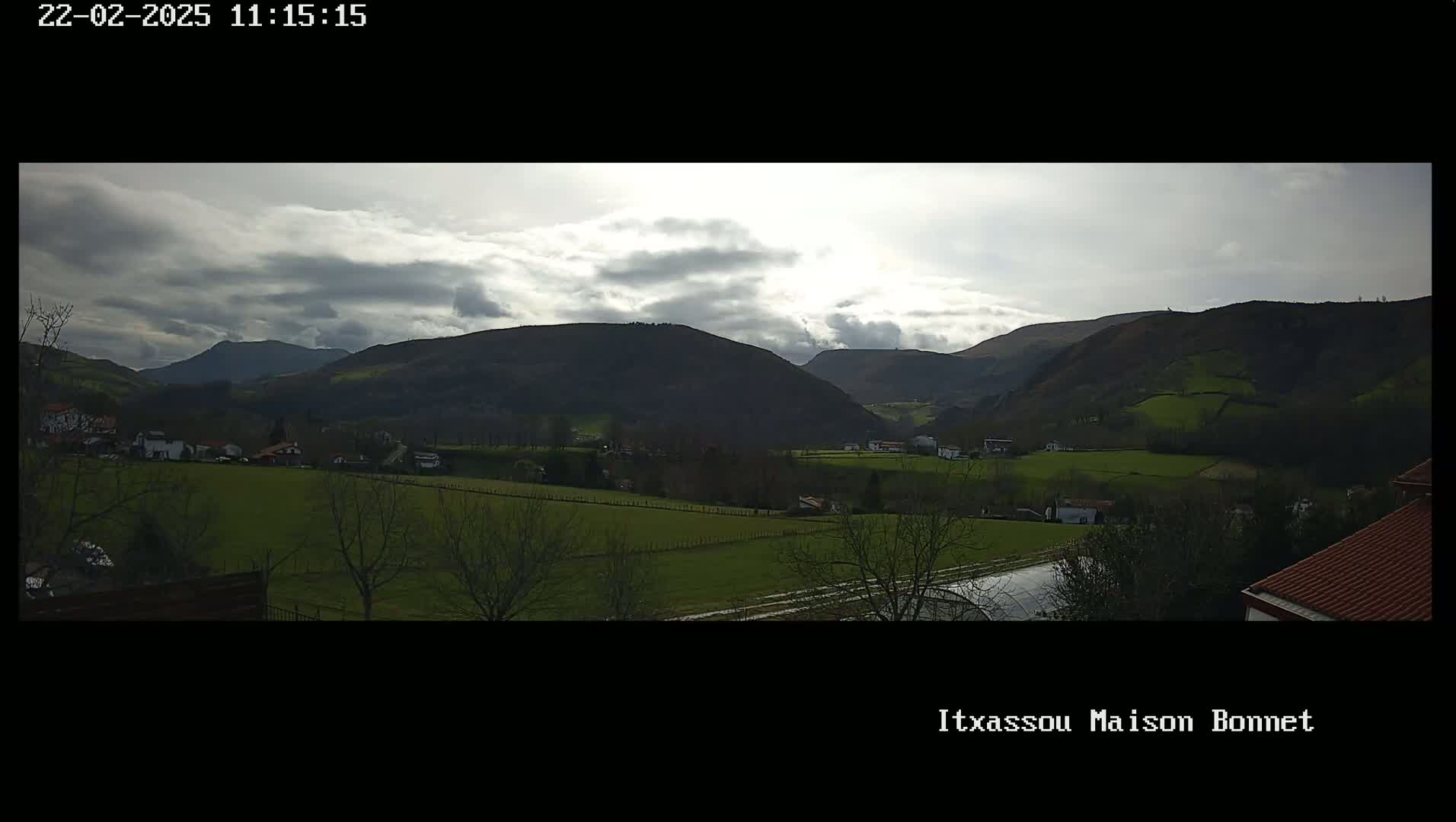 A partly cloudy day reveals a valley of green fields and scattered houses nestled among rolling hills.