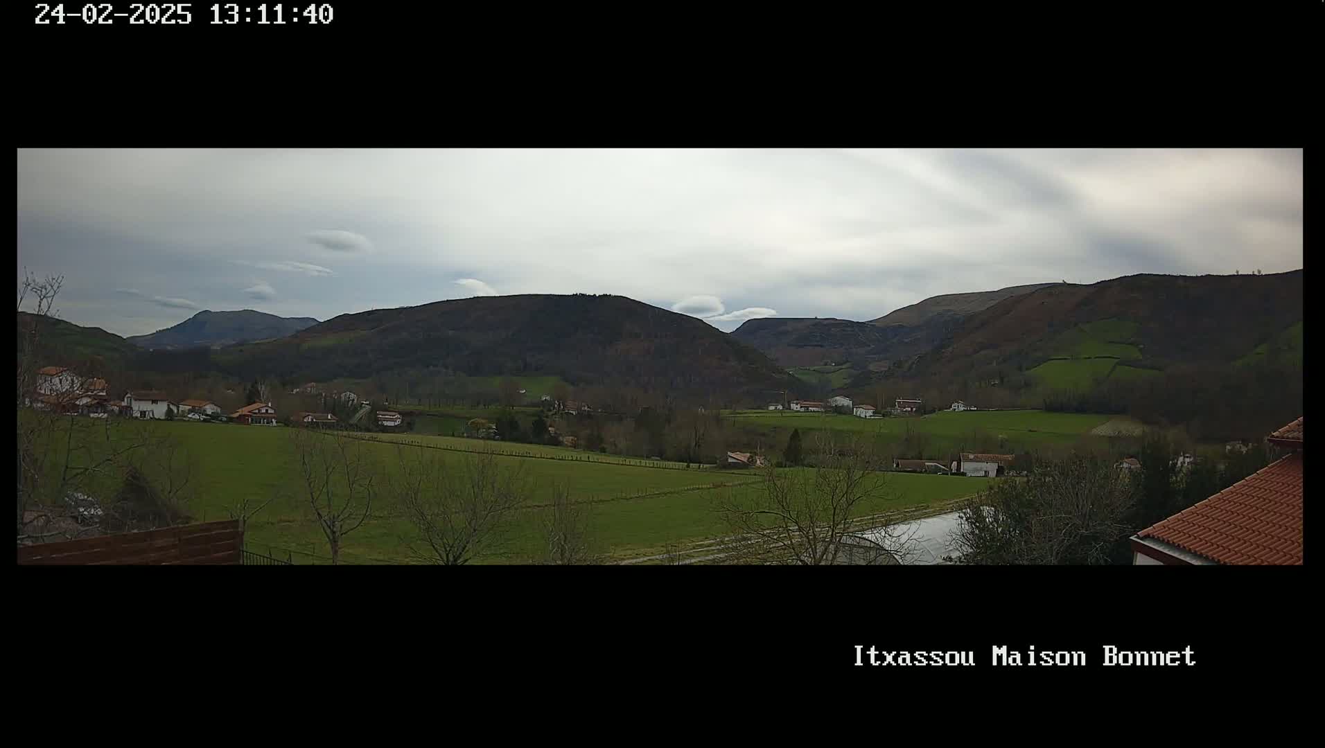 A panoramic view of a valley with several houses and farmlands under a cloudy sky.