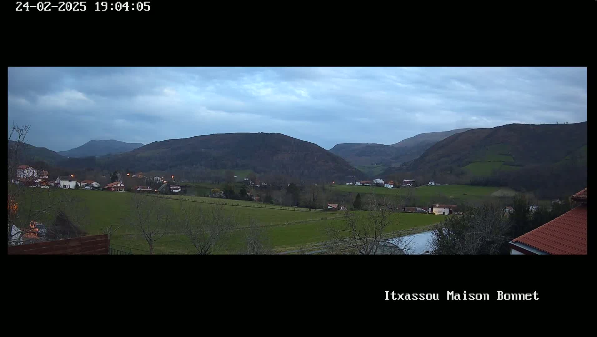 A tranquil valley scene at dusk shows a small village nestled among rolling green hills under a cloudy sky.