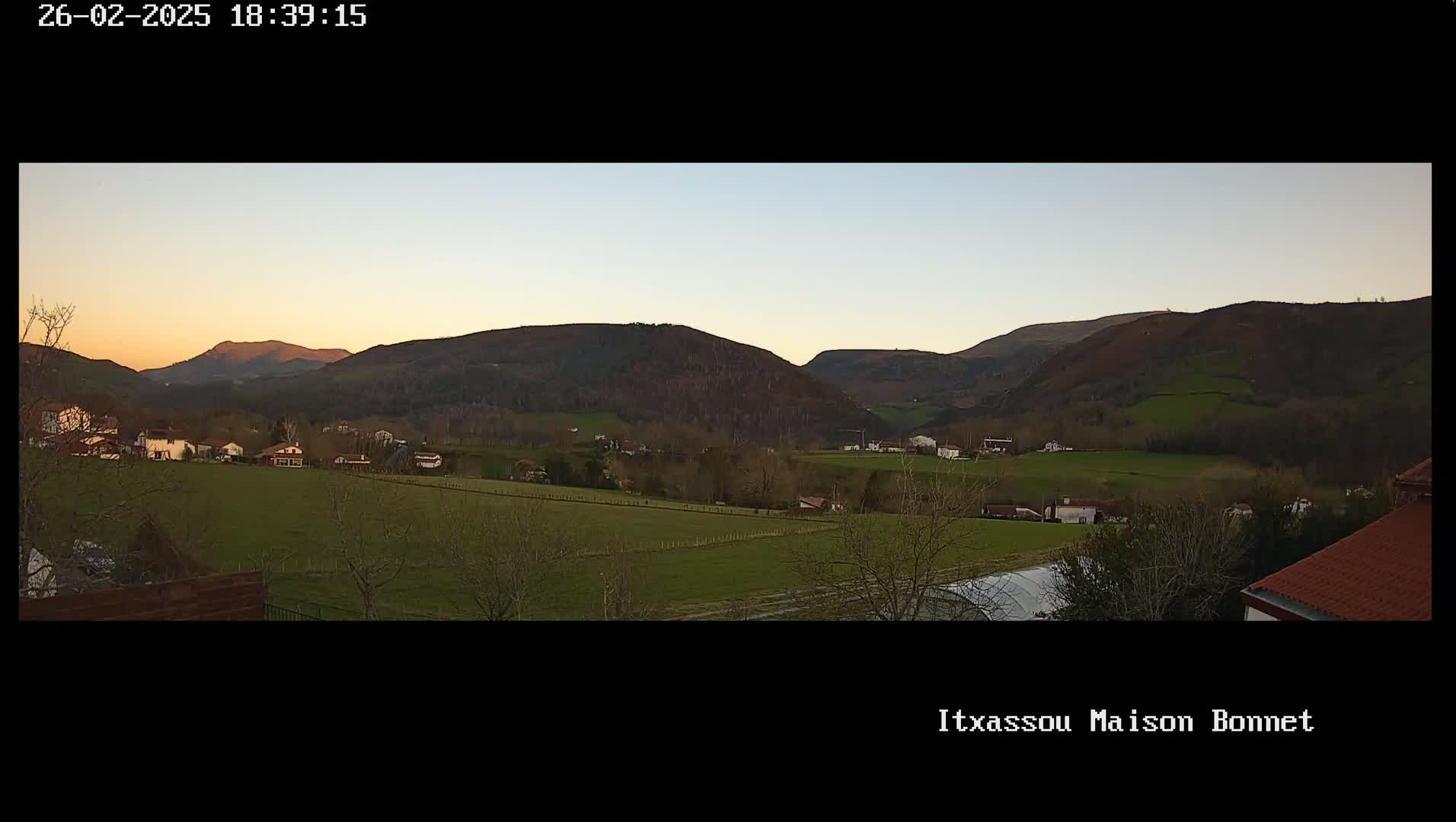 A tranquil sunset illuminates a pastoral valley dotted with houses and farmlands, nestled between gently rolling hills.