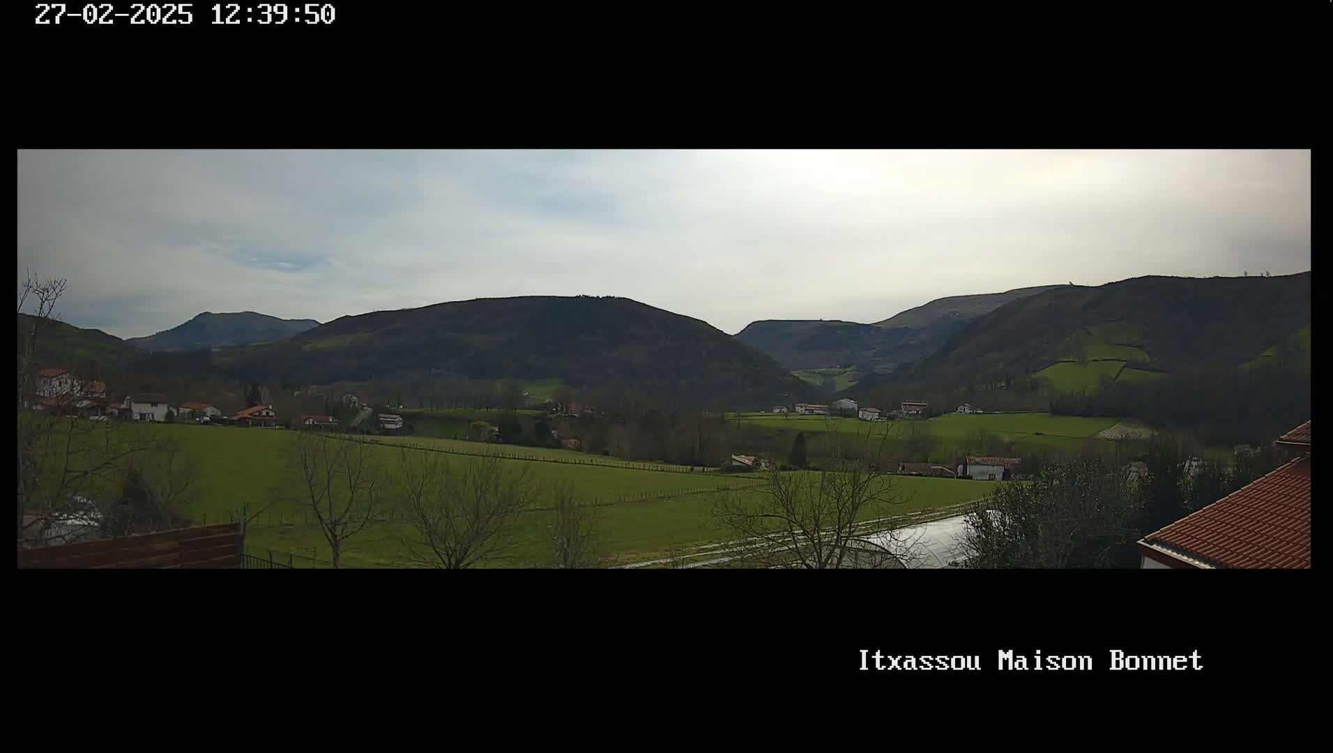 A panoramic view shows a valley of green fields and sparse trees under a mostly cloudy sky, with dark, rolling hills in the background.