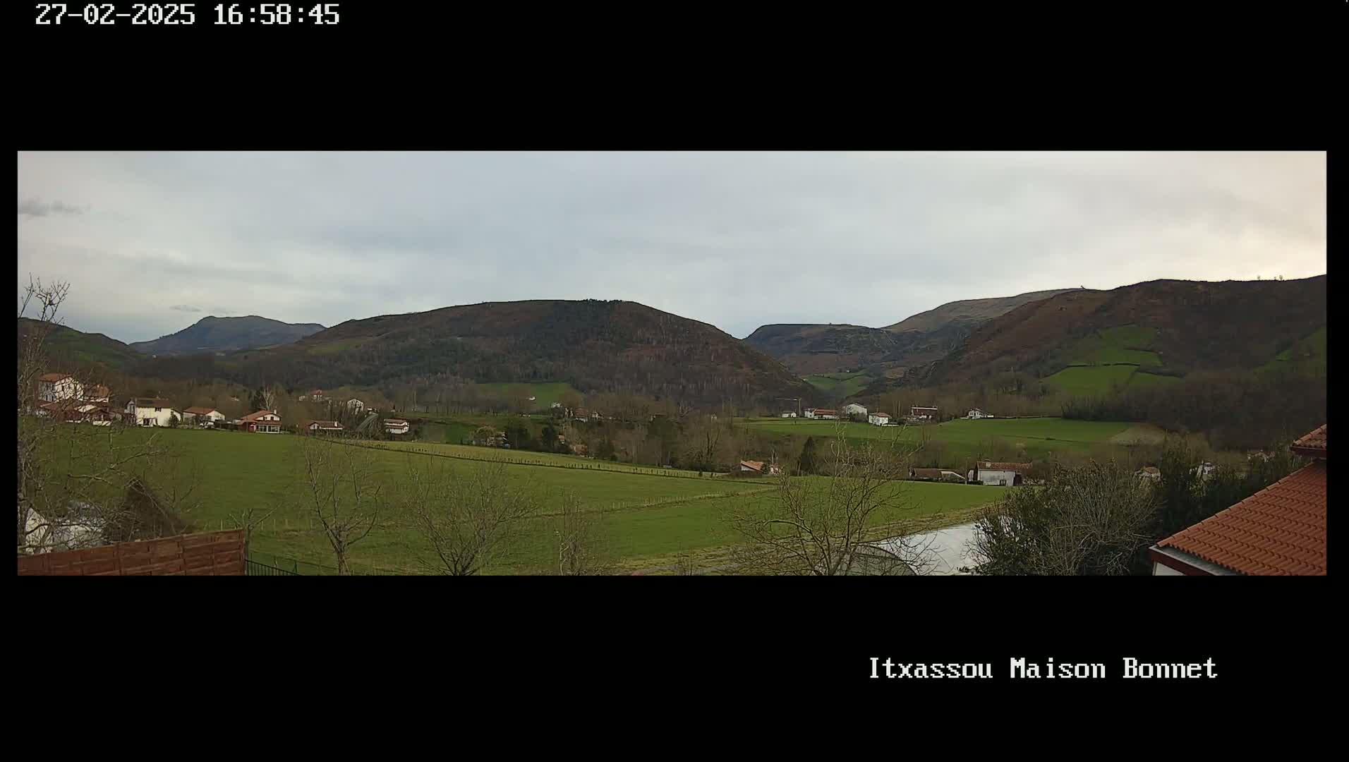 A panoramic view of a verdant valley dotted with houses under a cloudy sky, with rolling hills in the background.