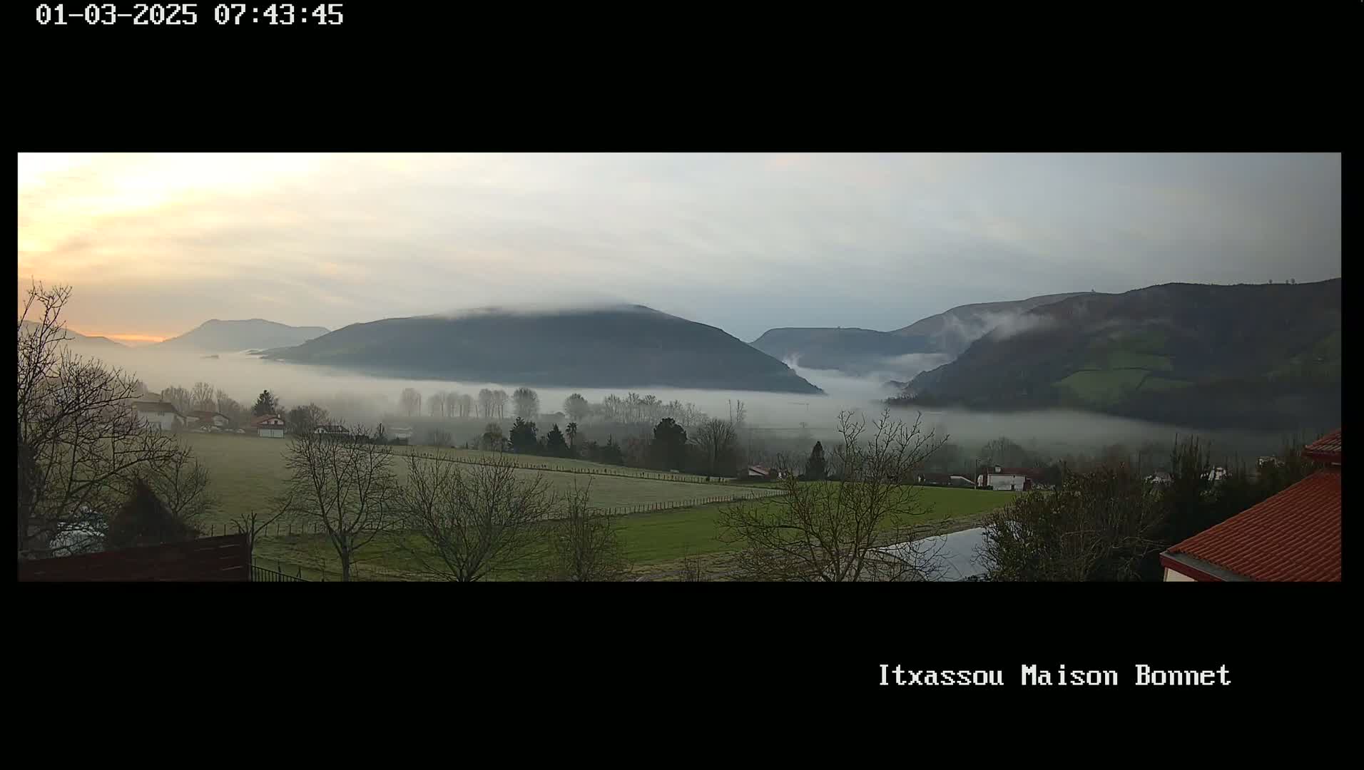 A foggy sunrise over a valley with low-lying houses and rolling hills.