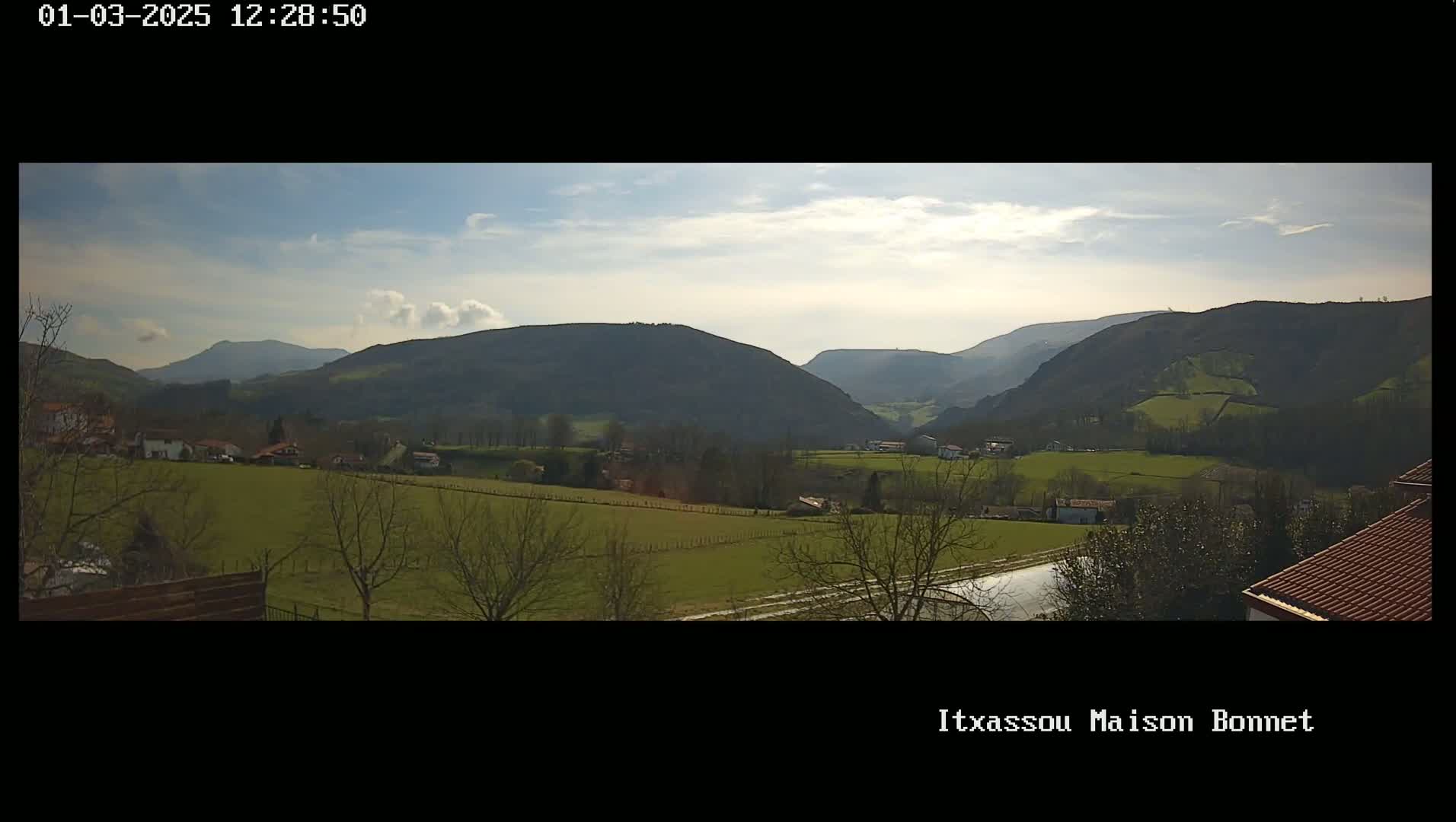 A sunny day reveals a panoramic view of rolling green hills and a valley dotted with houses, under a partly cloudy sky.