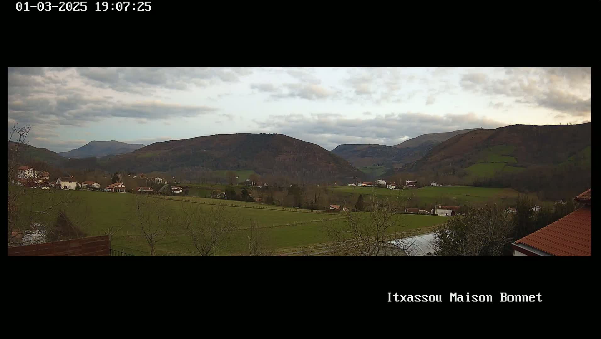 A cloudy day reveals a valley with a small village nestled among green fields and brown hills.