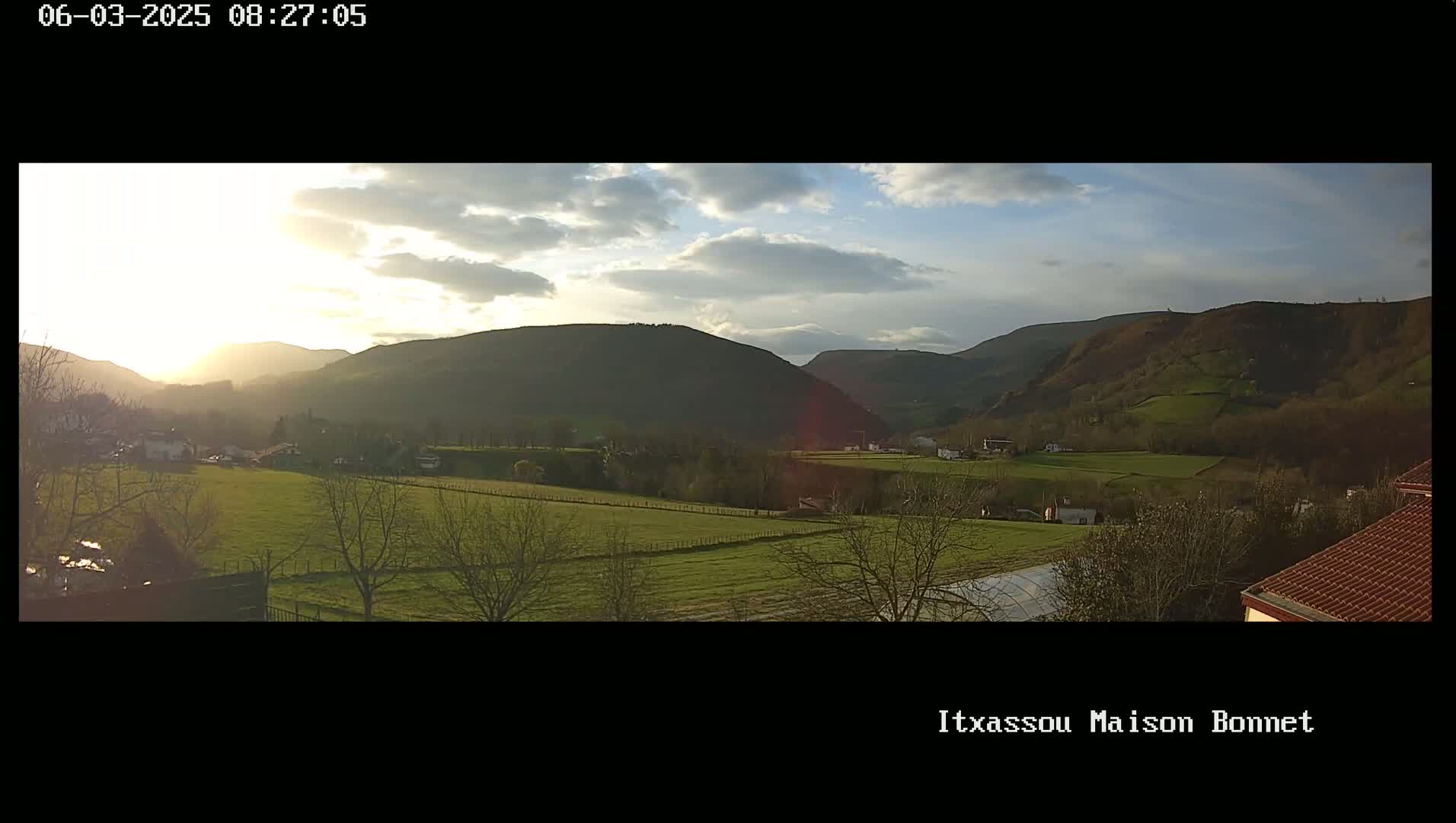 A partly cloudy sunset illuminates a valley of green fields and dark-green hills.