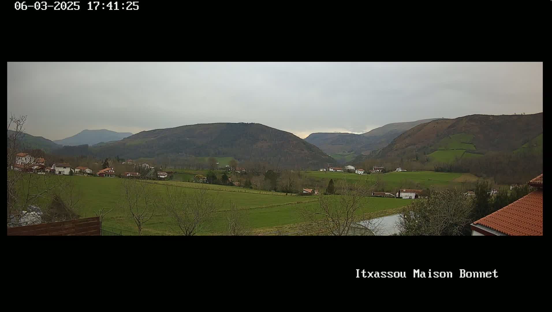 A valley dotted with houses and farmland under a cloudy sky stretches to rolling green hills in the distance.