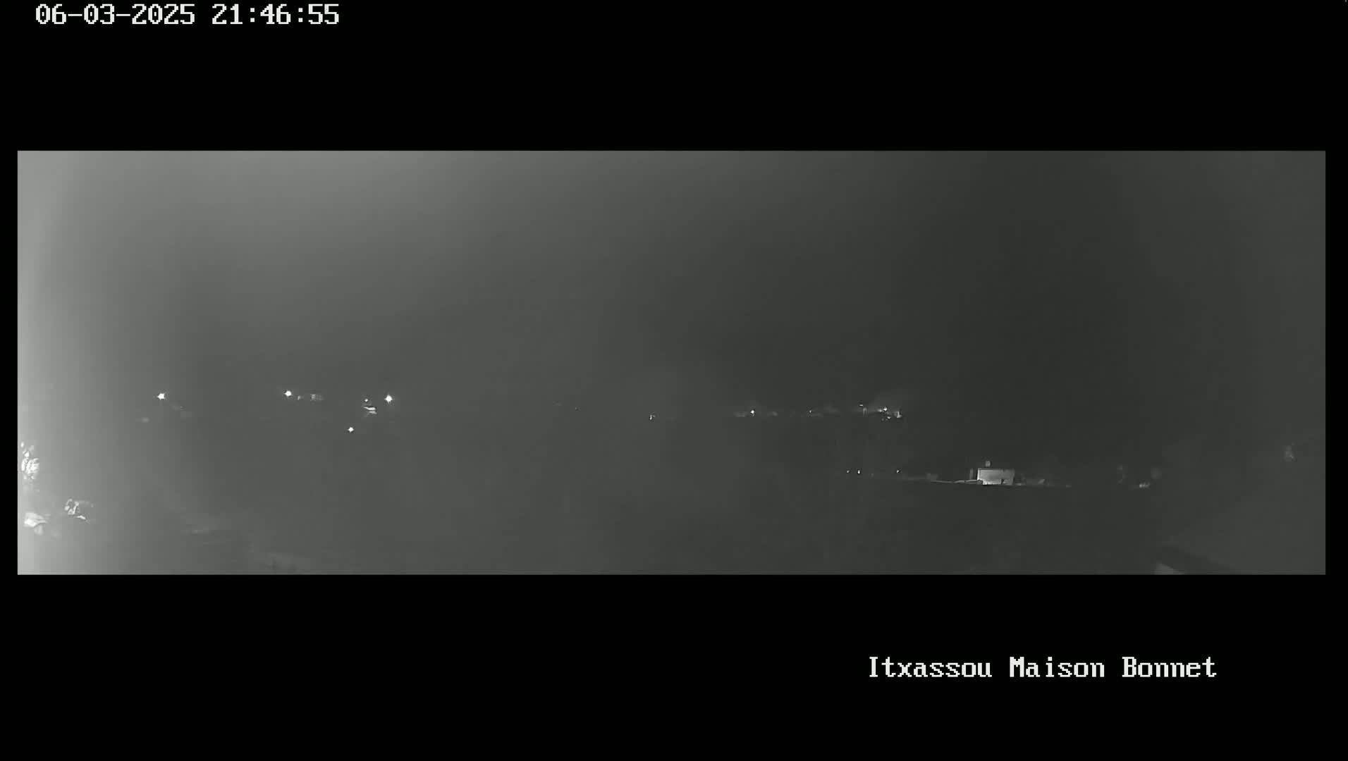 A nighttime, hazy, low-light view of a landscape showing a few faint lights in the distance.