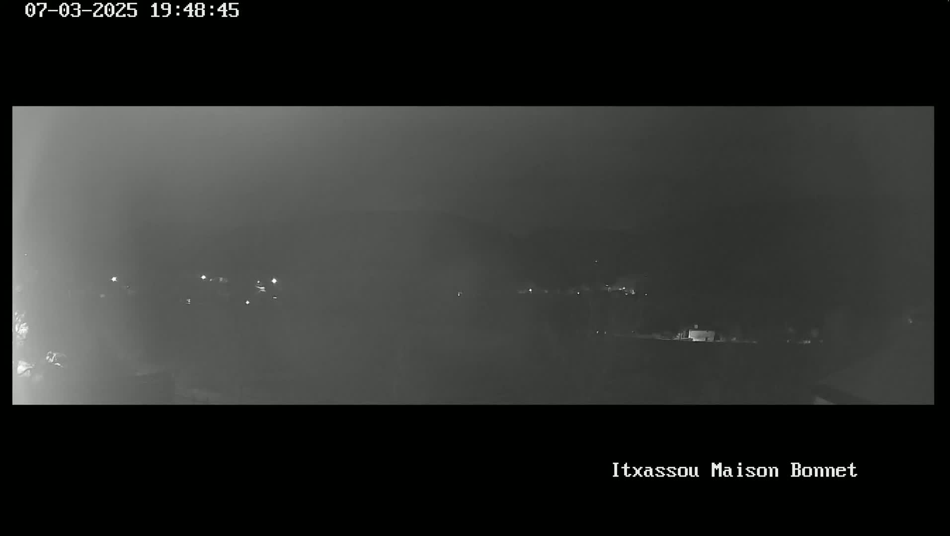 A nighttime, hazy view shows a distant line of dimly lit buildings or structures.